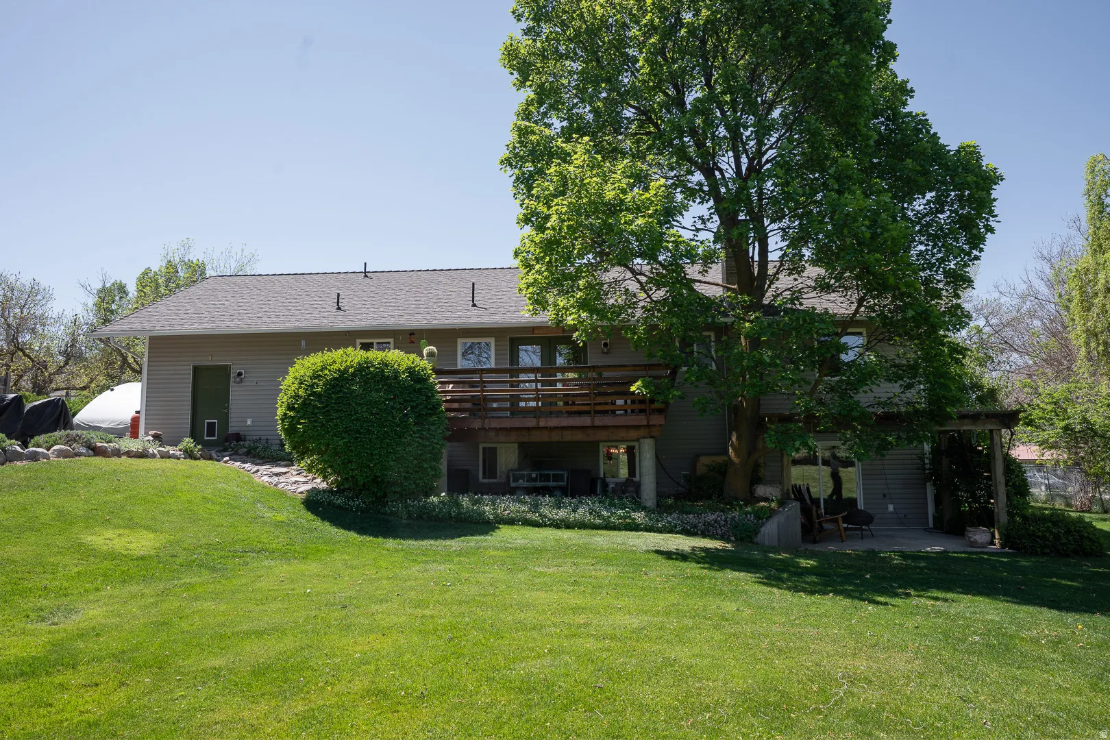 Rear exterior featuring a large wooden deck, lower-level patio space, and sloped lawn