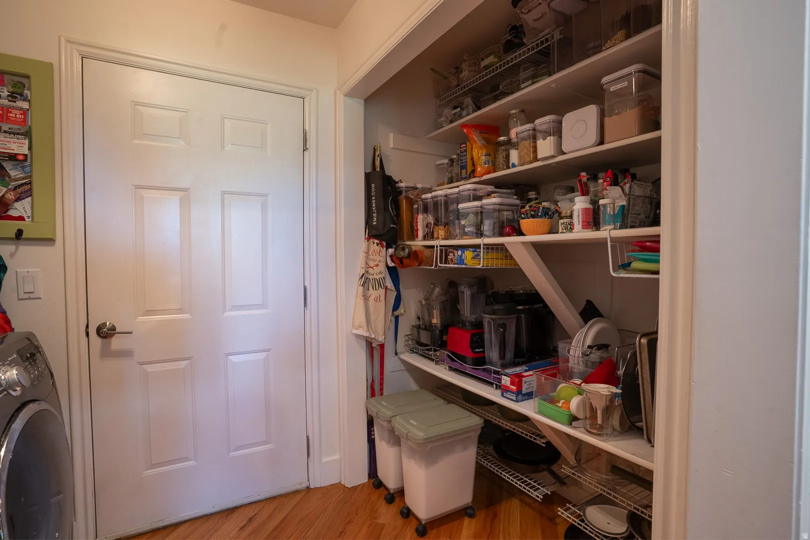 Pantry featuring built-in shelving, wire racks, and wood-finish flooring, across from the washer and dryer.