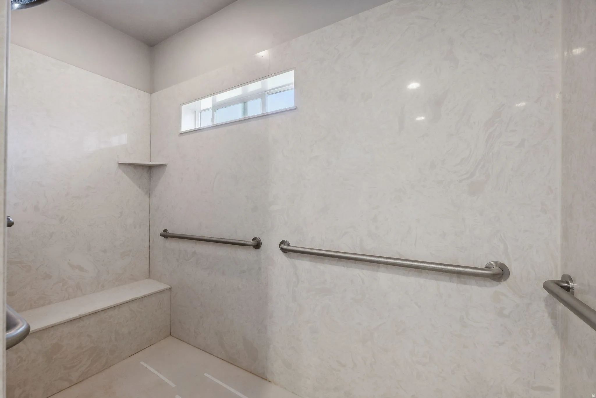 Expansive shower with light-toned wall panels, a built-in bench, and multiple grab bars