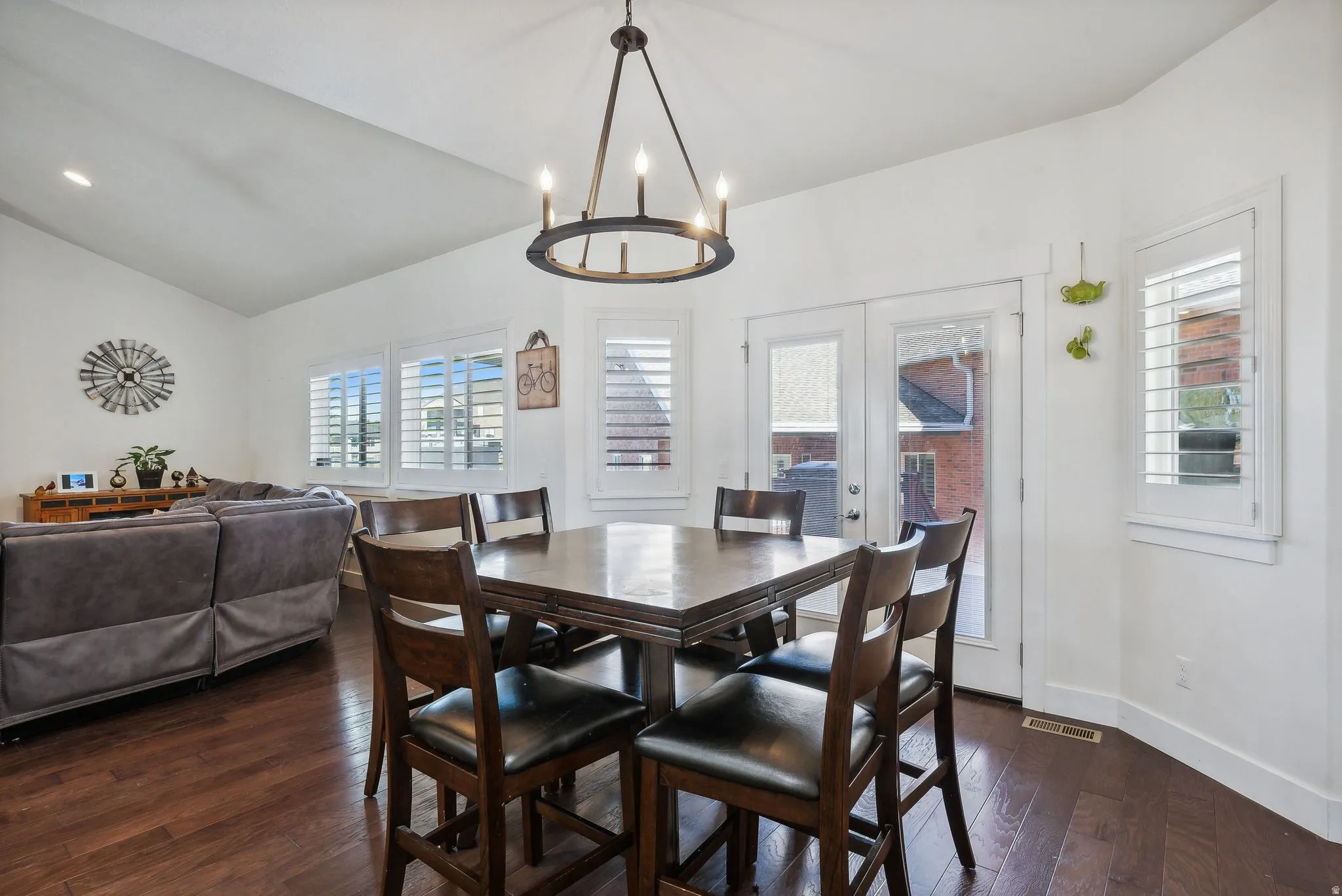 Spacious open-concept living area featuring a vaulted ceiling, dark wood-finish flooring, and white plantation shutters
