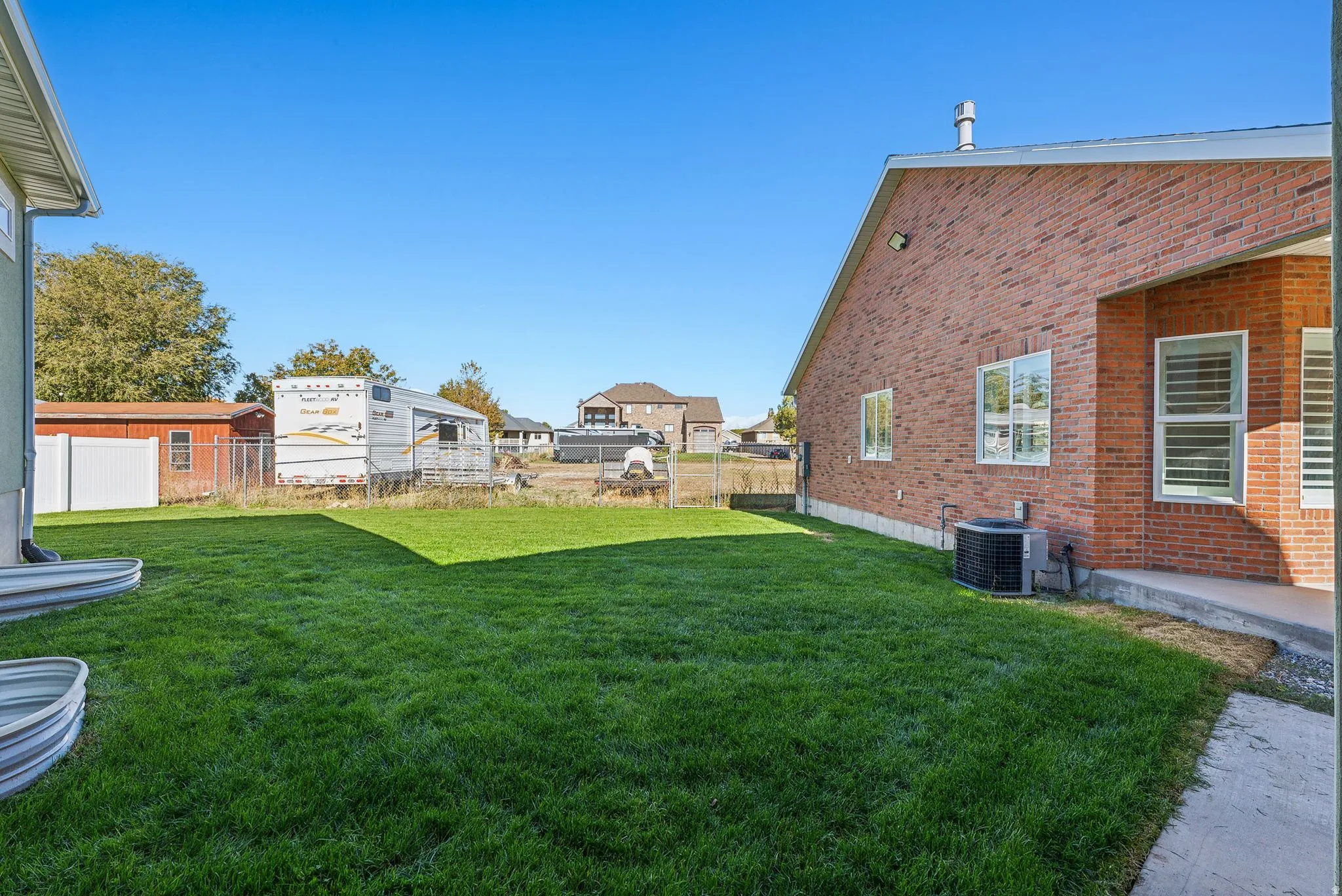 Expansive lawn area with a red brick exterior, a concrete patio, and multiple windows with white frames