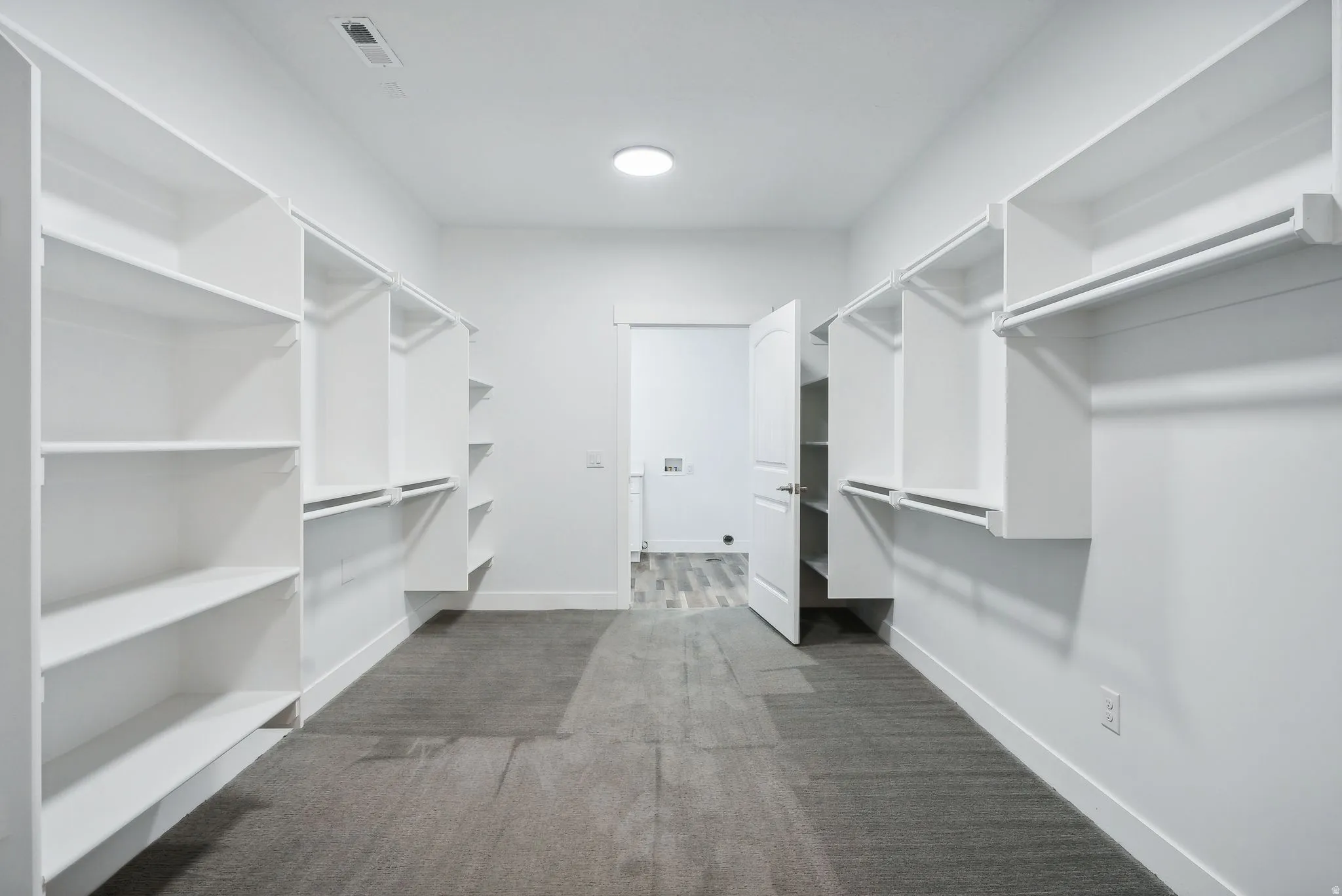 Custom built ADU/Spacious walk-in closet featuring extensive built-in shelving, hanging rods, and gray carpet flooring