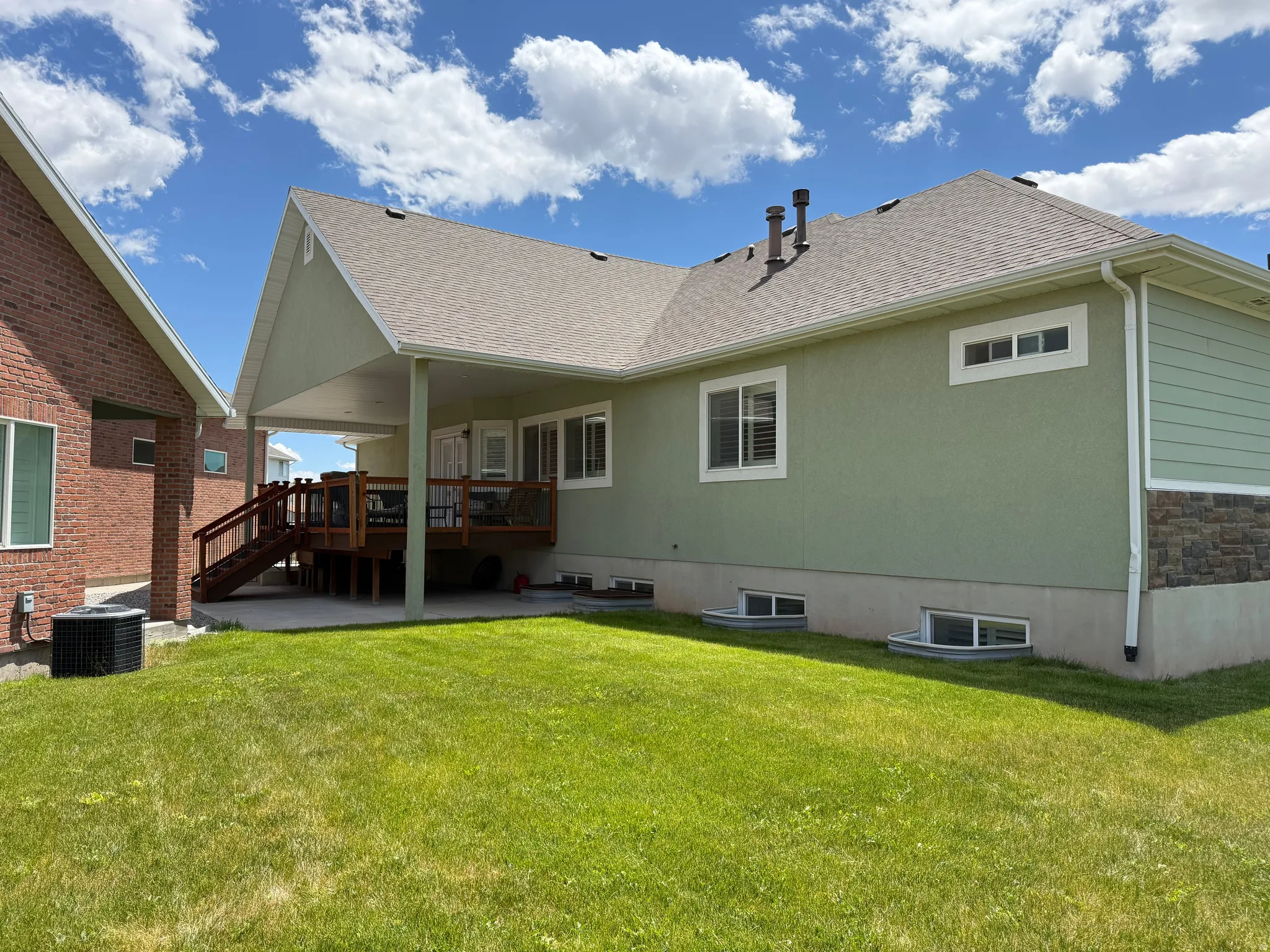Expansive backyard featuring a covered deck with stained wood railing, a concrete patio, and a manicured lawn