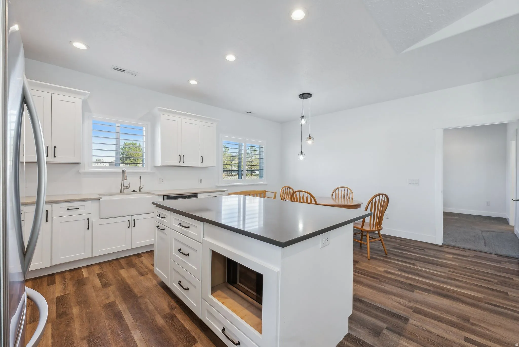 Custom built ADU/Modern kitchen featuring a central island with dark countertop, white cabinetry with black hardware, wood-finish flooring, a farmhouse sink, and recessed lighting