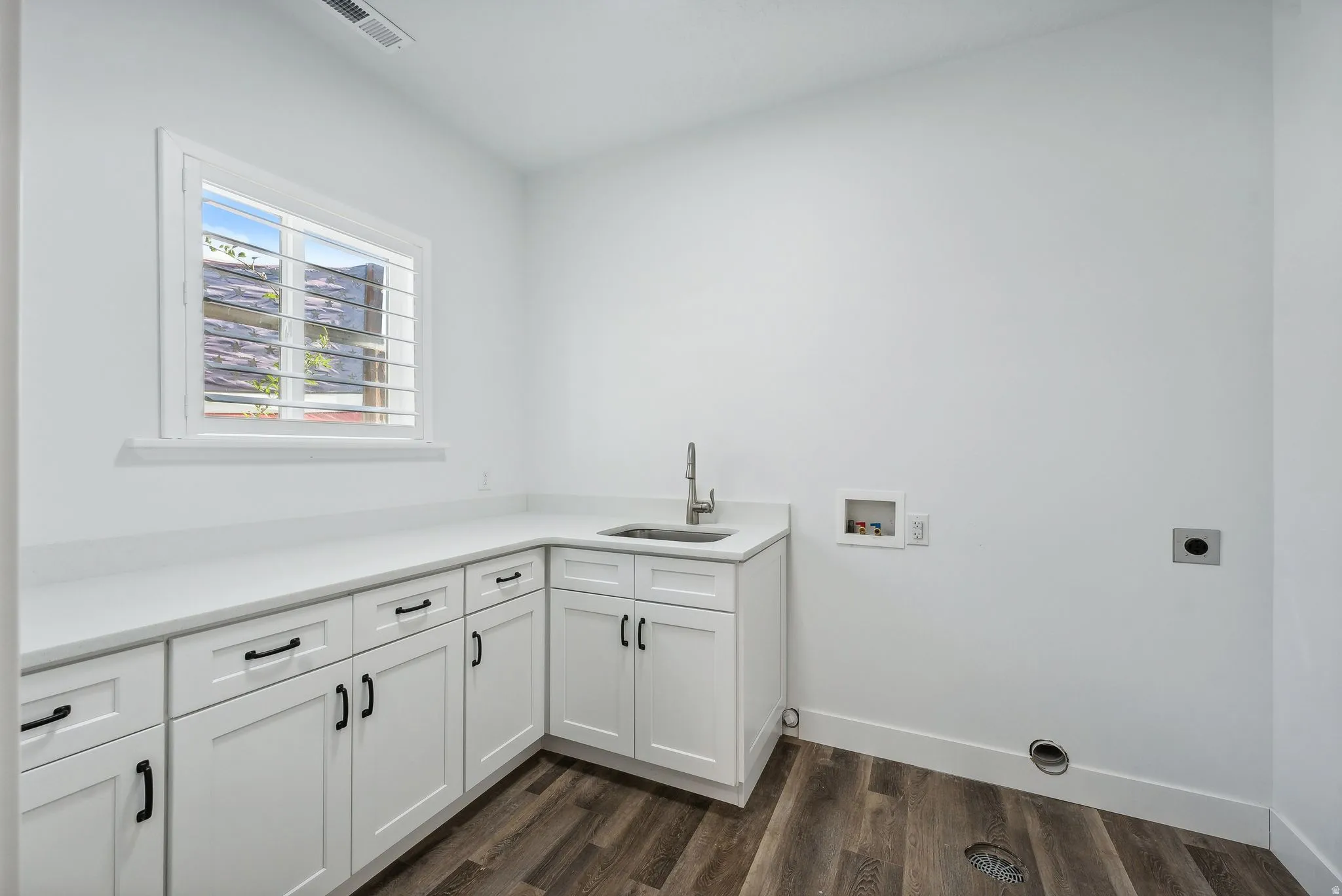 Custom built ADU/Utility room with a corner sink, extensive white cabinetry, a light-toned countertop, and wood-finish flooring