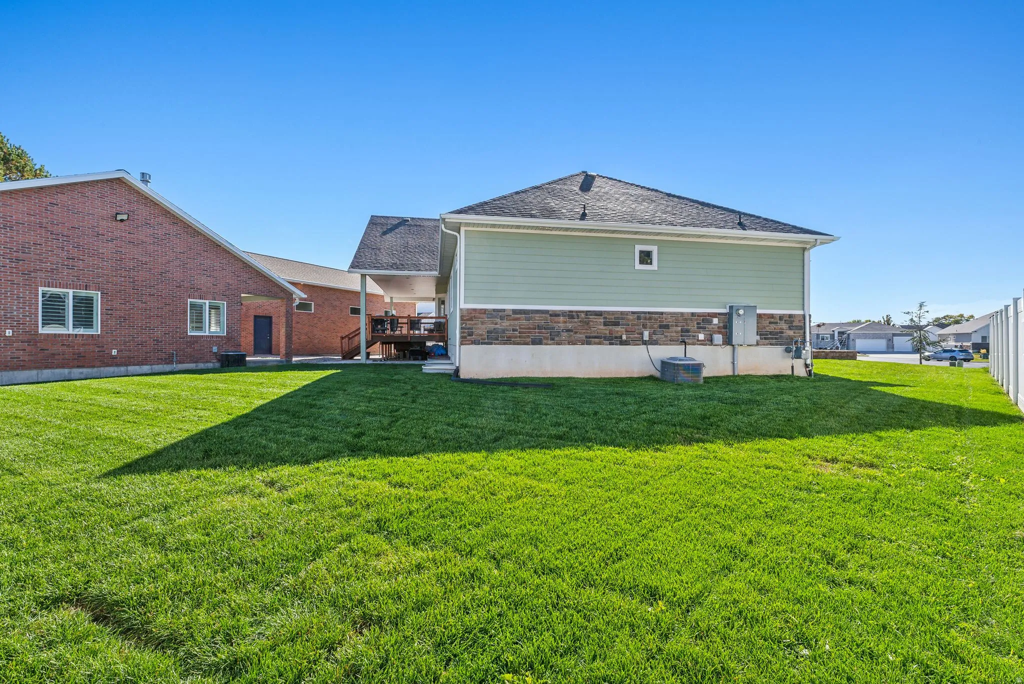 Expansive green lawn with a two-story residence featuring light green siding and a stone facade