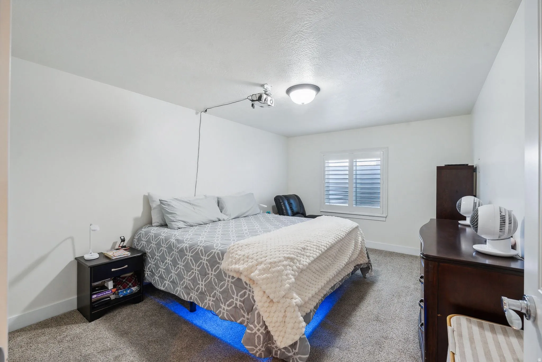 Bedroom featuring light gray carpet flooring, white walls, and a window with white louvered shutters