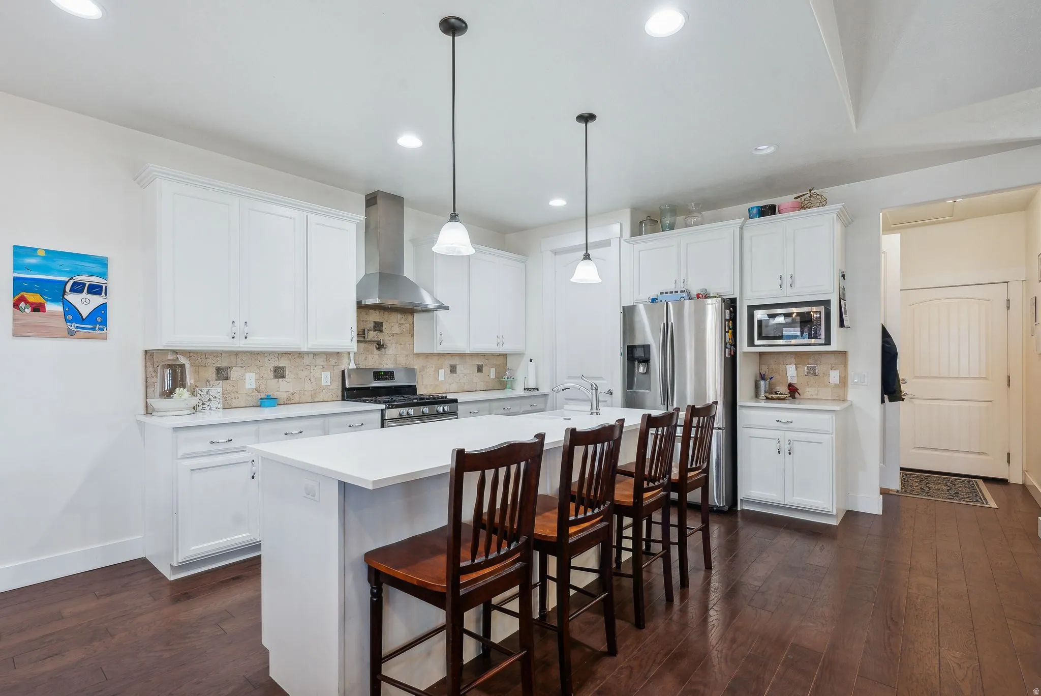 Spacious kitchen featuring an expansive central island with seating, white shaker-style cabinetry, stainless steel appliances, and wood-finish flooring
