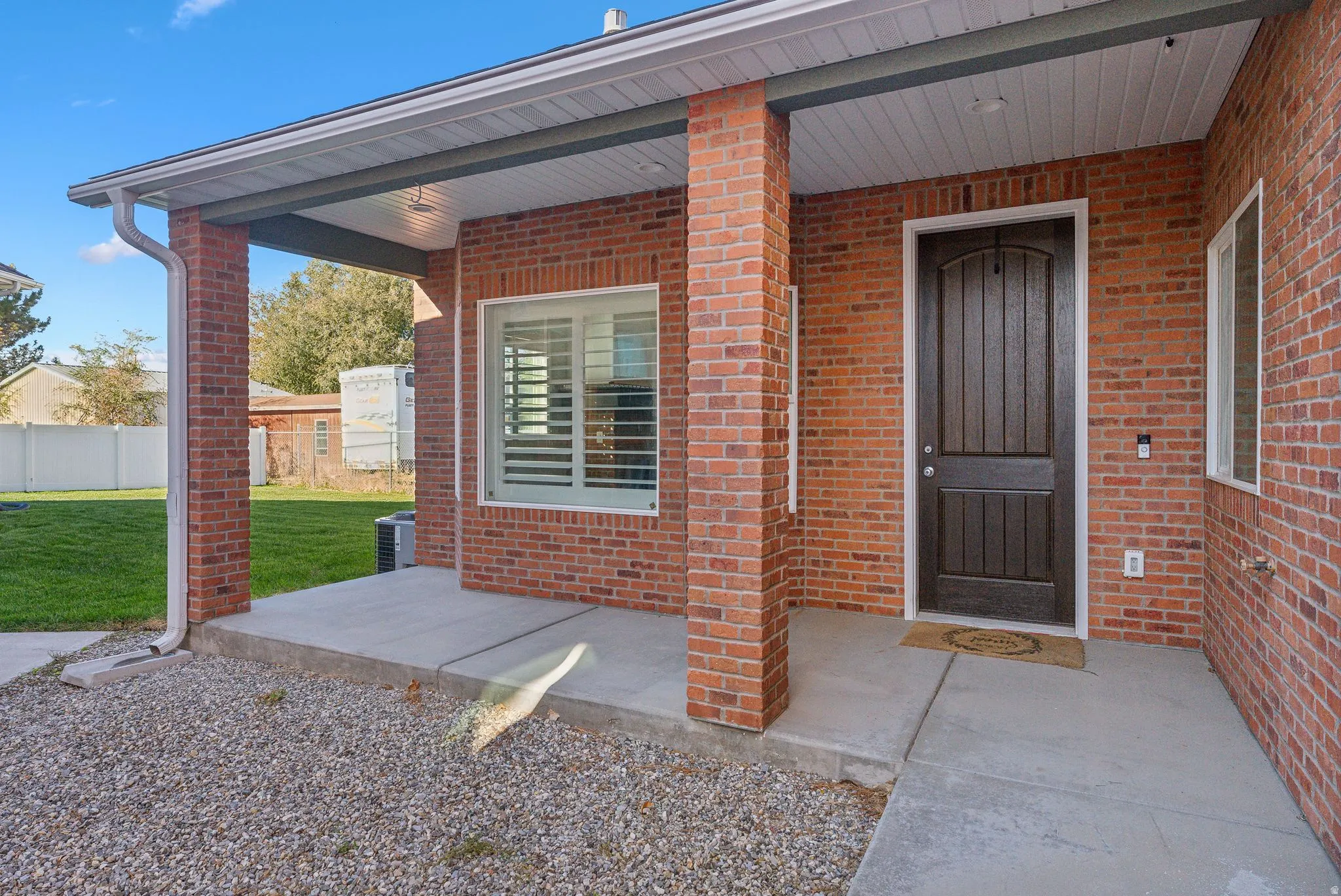 Custom built ADU/Brick exterior featuring a covered entry porch with recessed lighting, a dark wood-finish front door, and a window with white plantation shutters