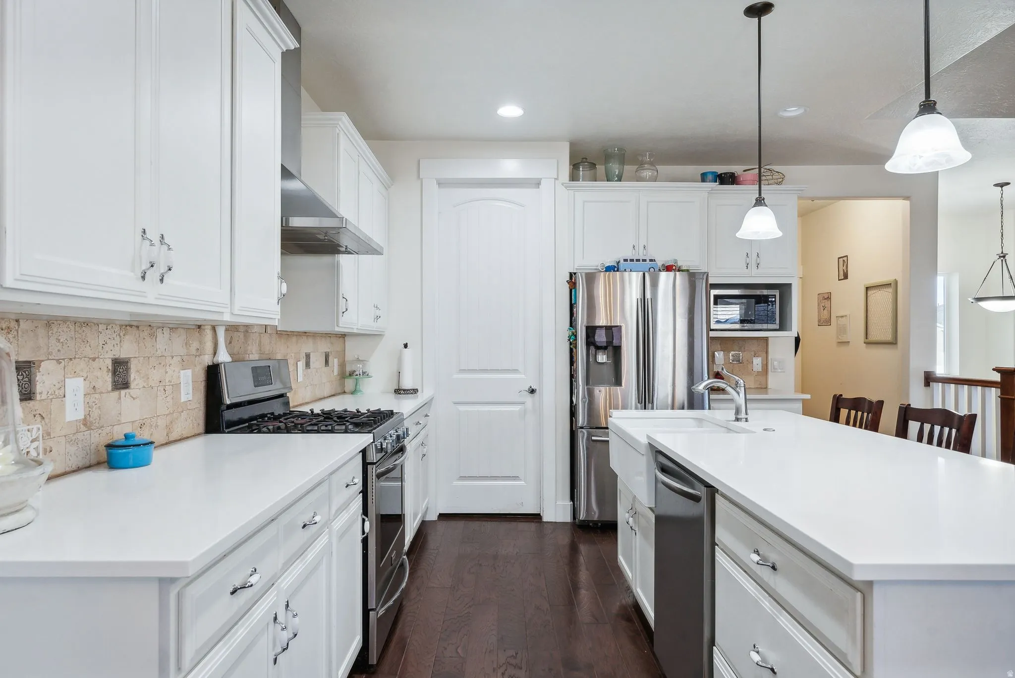 Modern kitchen featuring white cabinetry, light-toned countertops, stone backsplash, a stainless steel gas range, and wood-finish flooring