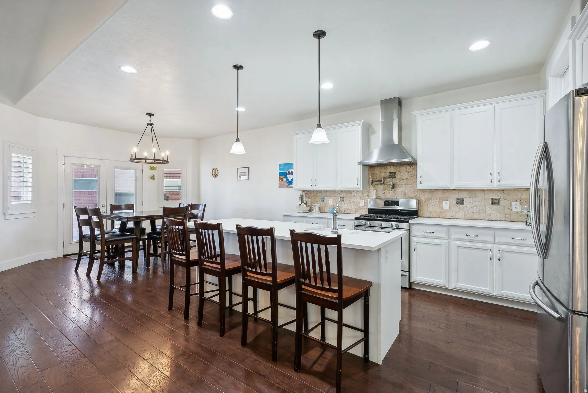 Open-concept kitchen featuring white cabinetry, stainless steel appliances, a center island with pendant lighting, and dark wood-finish flooring