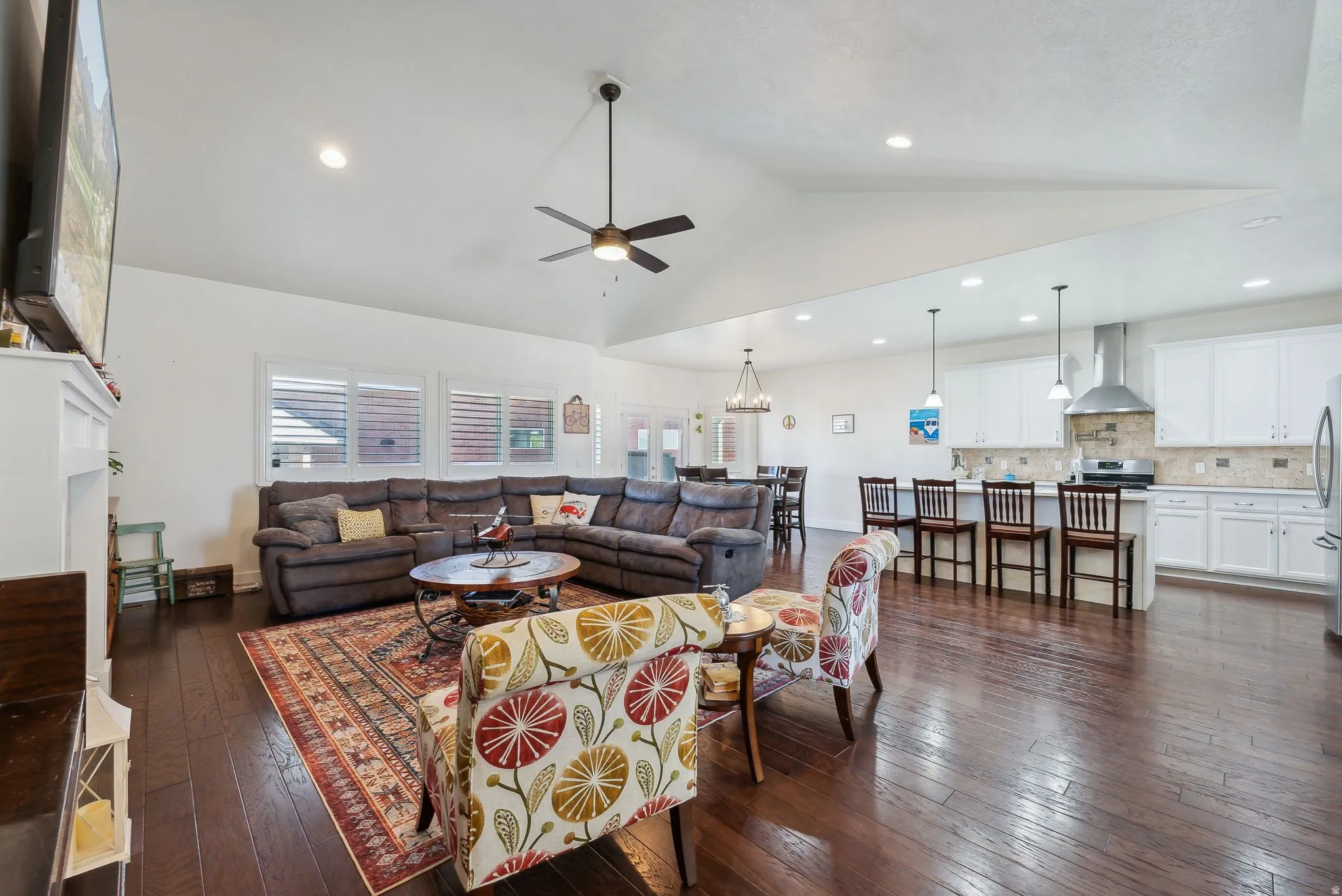 Spacious open-concept living area featuring wood-finish flooring, vaulted ceilings, and a ceiling fan