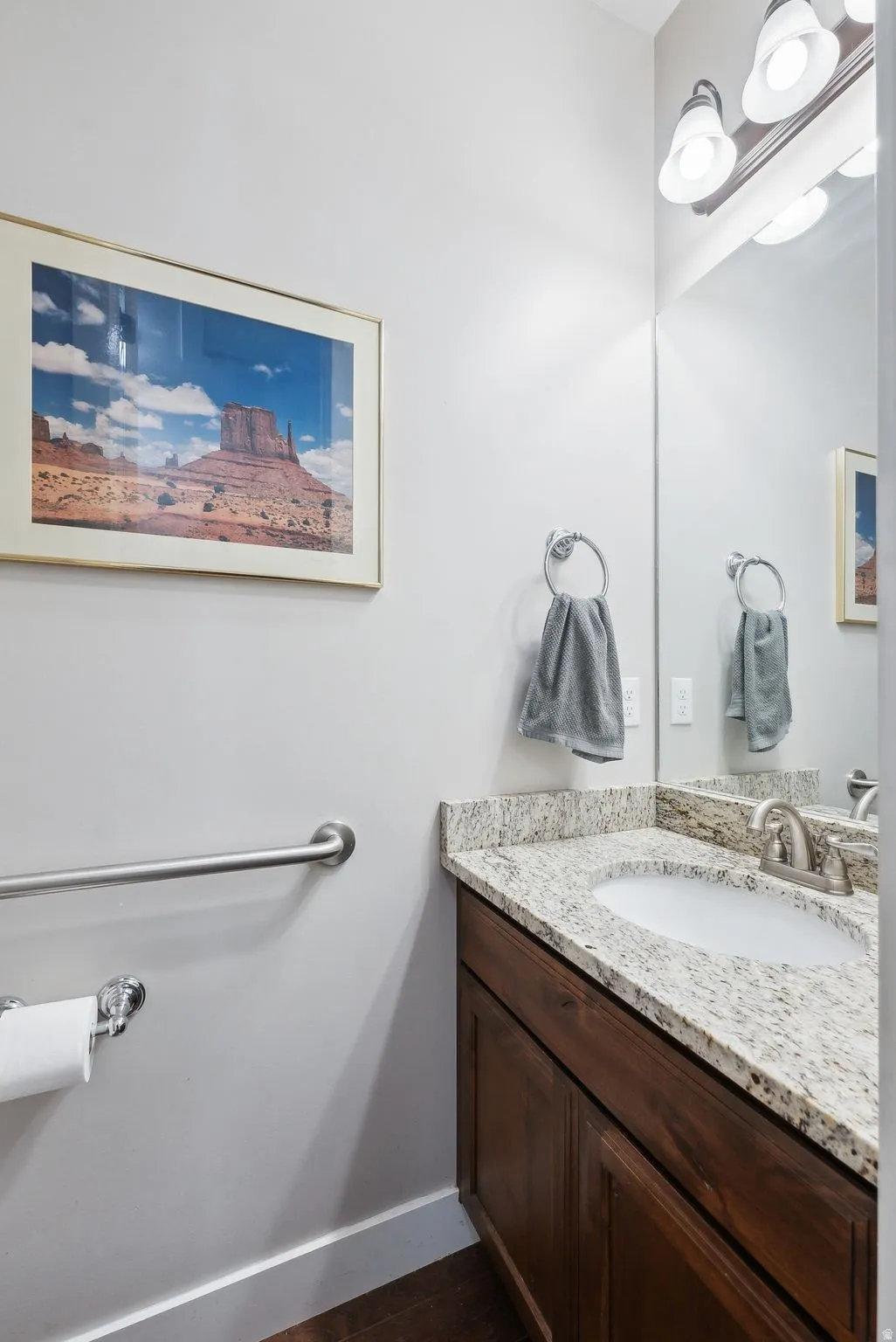 Powder room featuring a wood-finish vanity with an integrated sink, stone countertop, brushed nickel faucet, and overhead vanity lighting