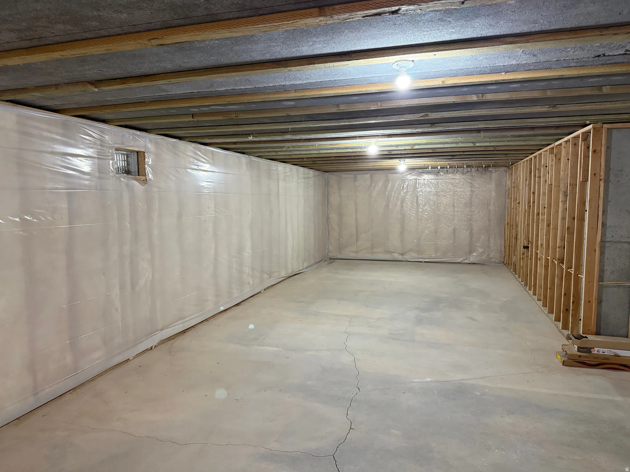 Unfinished basement featuring exposed ceiling joists, concrete flooring, vapor barrier wall covering, and partial wood framing for future development