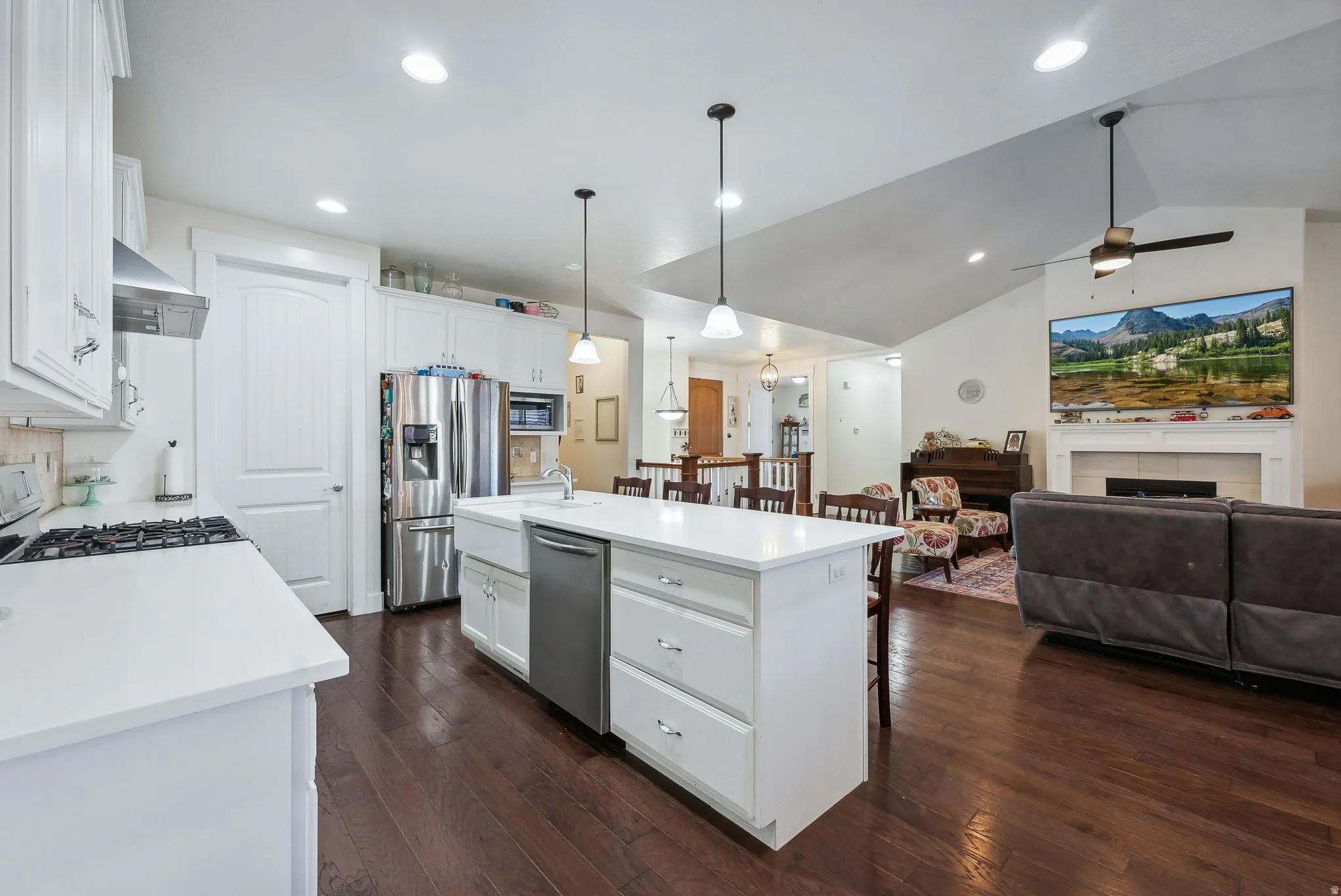 Open-concept kitchen and living area featuring a central island with countertop seating, stainless steel appliances, white cabinetry, and wood-finish flooring