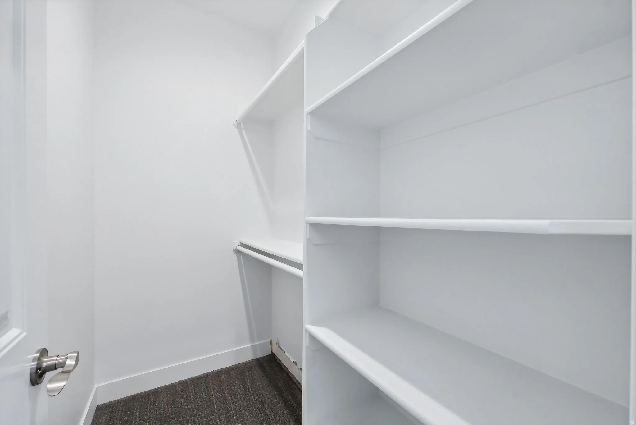 Custom built ADU/Walk-in closet featuring built-in shelving, white walls, dark gray carpet, and a white interior door with brushed nickel hardware