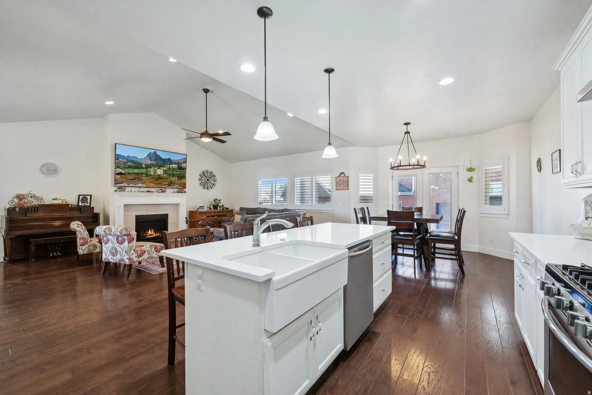 Open-concept living space featuring wood-finish flooring, a kitchen island with a farmhouse sink, white cabinetry with quartz countertops, and a fireplace with a mantel
