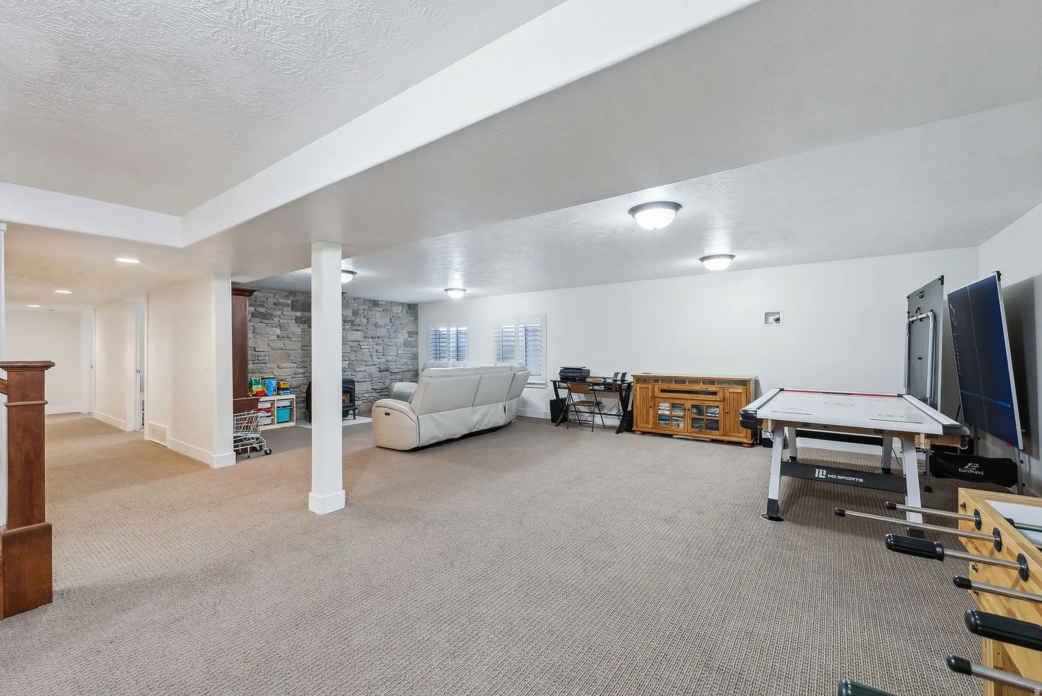 Expansive lower-level space featuring carpet flooring, recessed lighting, and a stone-clad fireplace