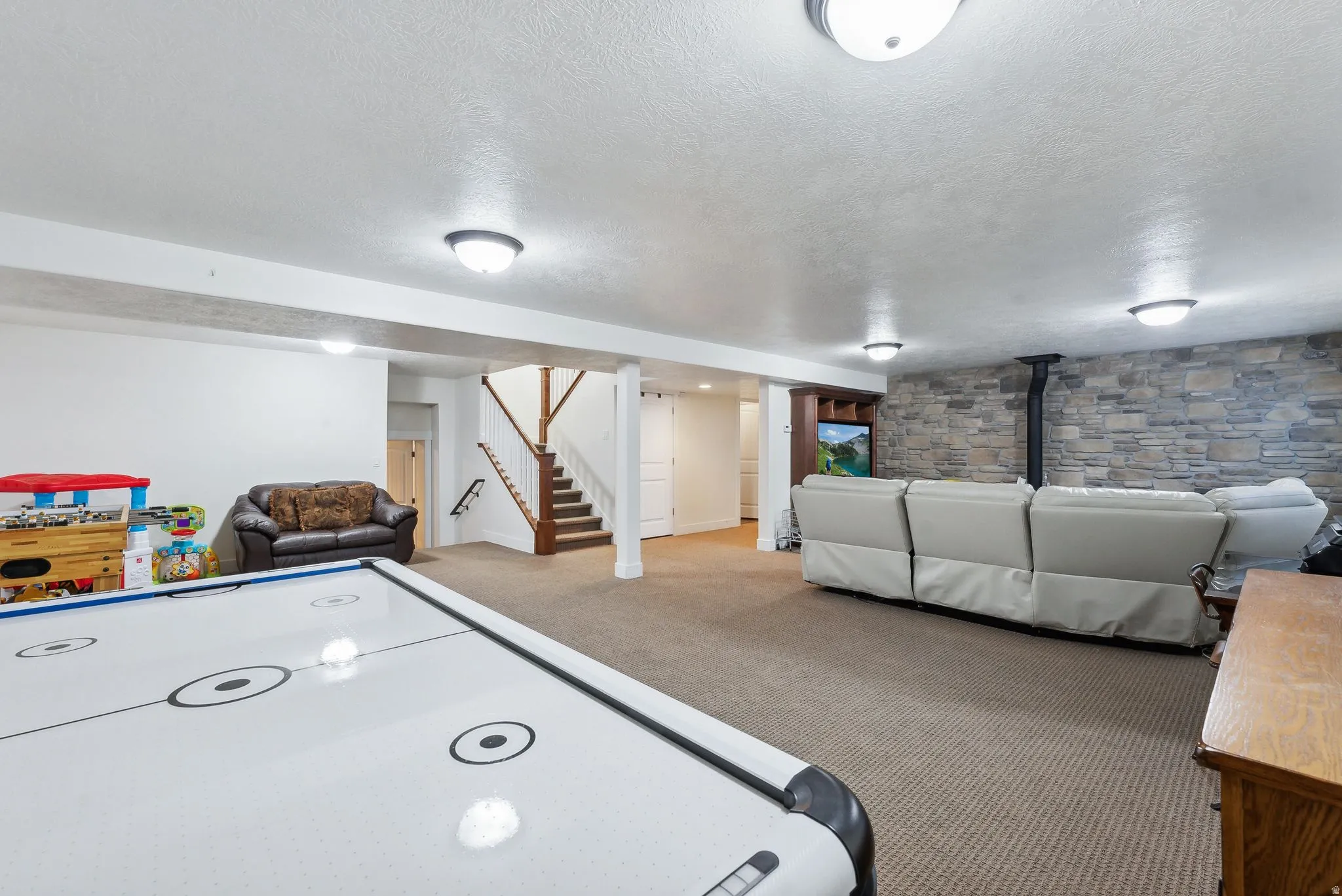 Finished basement space featuring carpeted flooring, a stone-accented wall, recessed lighting, and a built-in entertainment center