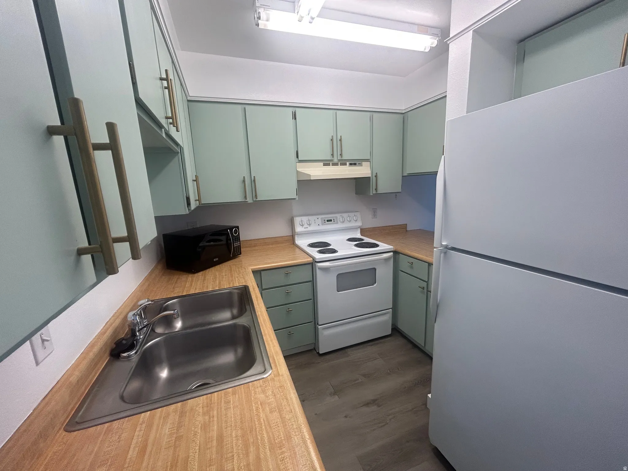 Kitchen featuring mint green cabinetry with gold-tone hardware, wood-finish countertops, stainless steel double basin sink, white electric range with overhead ventilation, and a white refrigerator