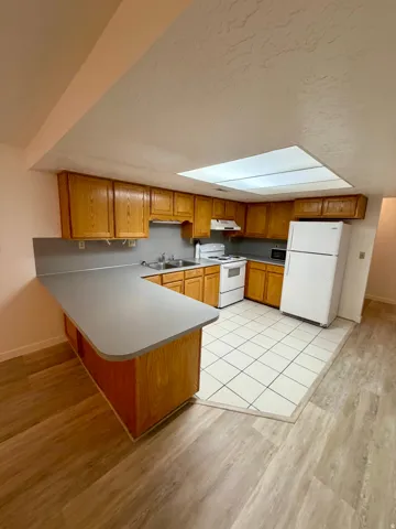 Kitchen featuring wood cabinetry, white appliances, a tile backsplash, and a breakfast bar