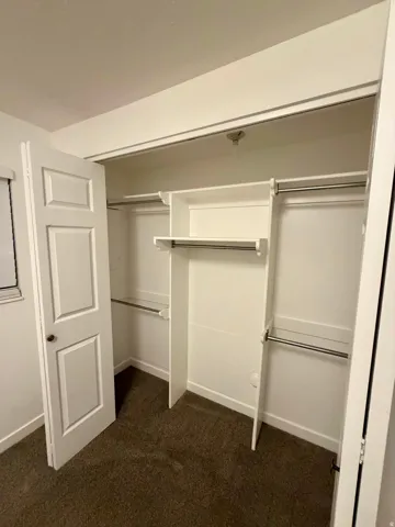 Closet interior featuring built-in shelving, multiple hanging rods, and dark carpeting