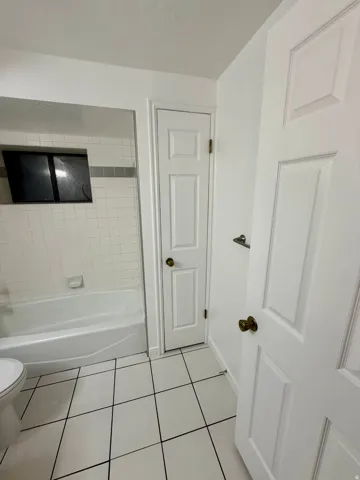 Bathroom featuring white subway tile with a gray accent stripe, a white bathtub, and white floor tiles with dark grout