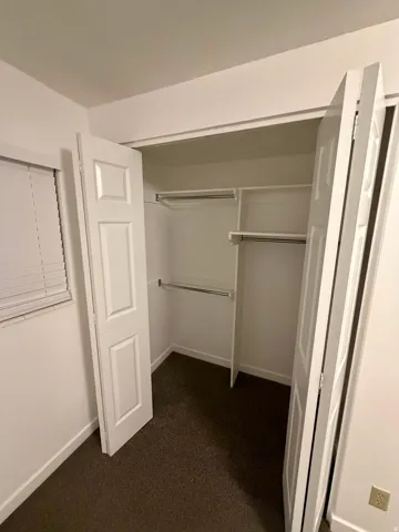 Spacious closet featuring bi-fold panel doors, upper and lower hanging rods, integrated shelving, and dark textured carpeting