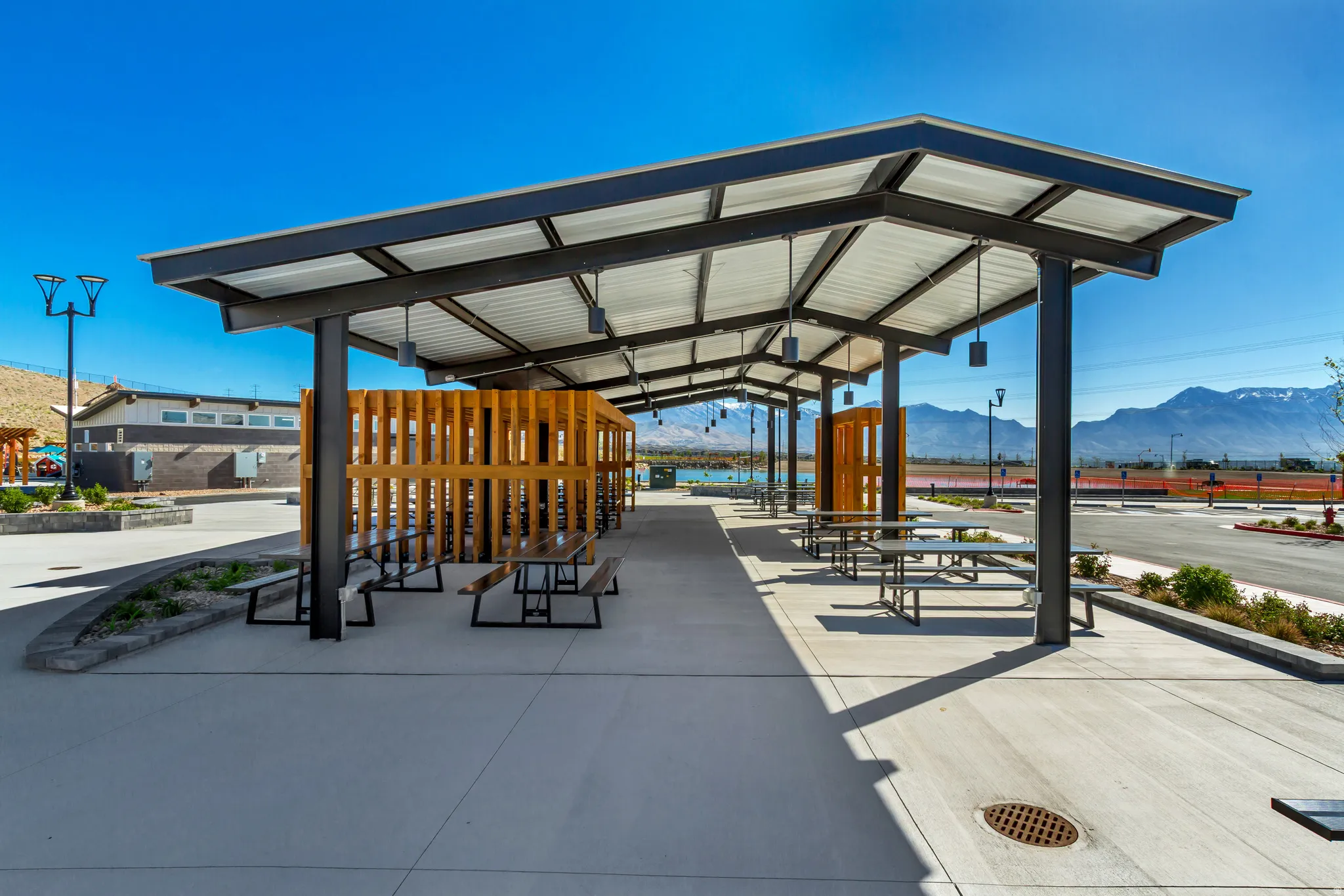 Covered outdoor seating area featuring a metal roof structure, wood-slat privacy walls, and multiple picnic tables