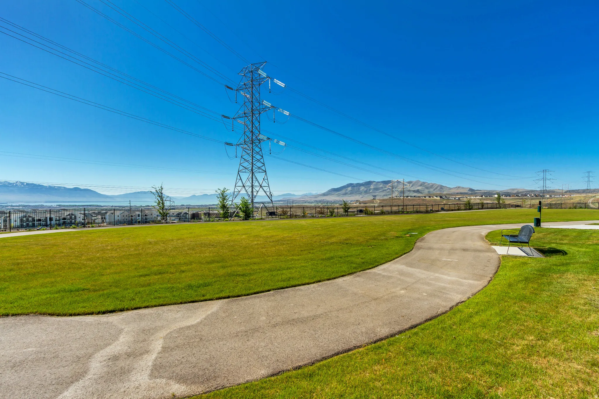 Expansive green space featuring a paved walking path, mountain backdrop, and distant body of water