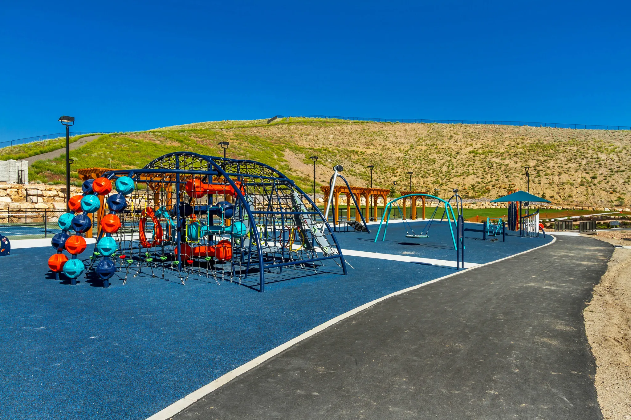 Spacious outdoor recreation area featuring a soft-surface playground with climbing structures, swings, and shade canopy