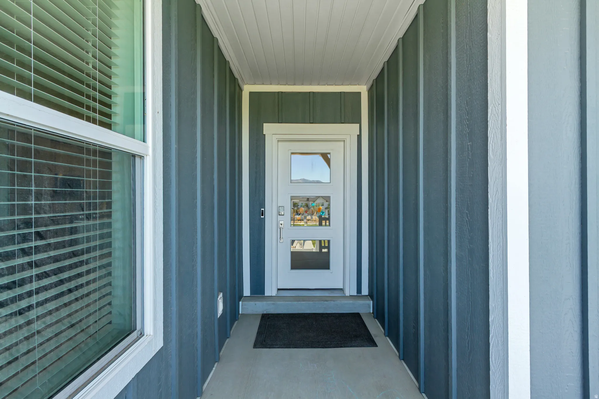 Covered entry featuring a modern white door with three glass inserts, vertical board and batten siding, and white trim accents