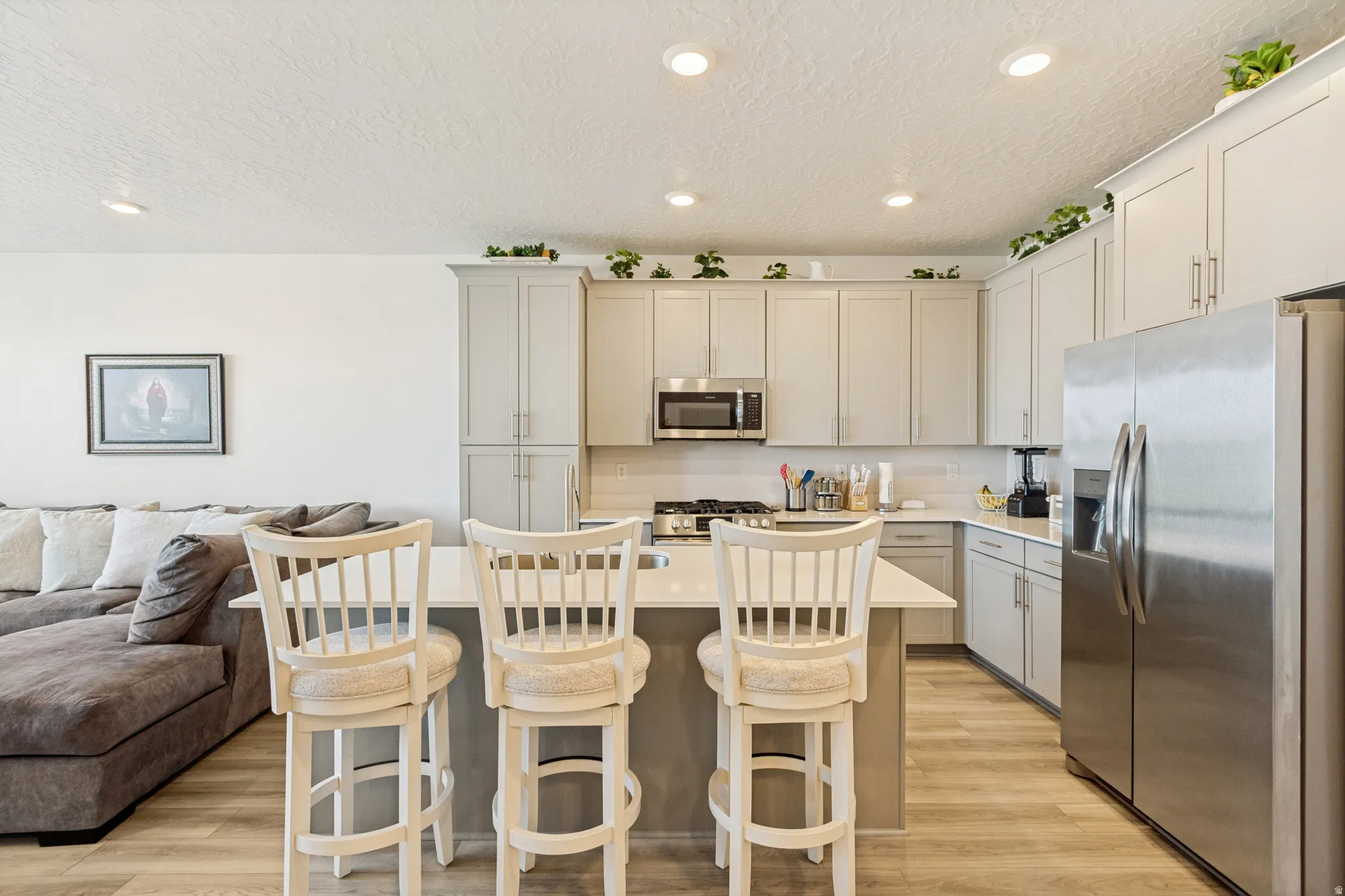 Modern kitchen featuring light gray cabinetry, stainless steel appliances, a white subway tile backsplash, and light wood-finish flooring