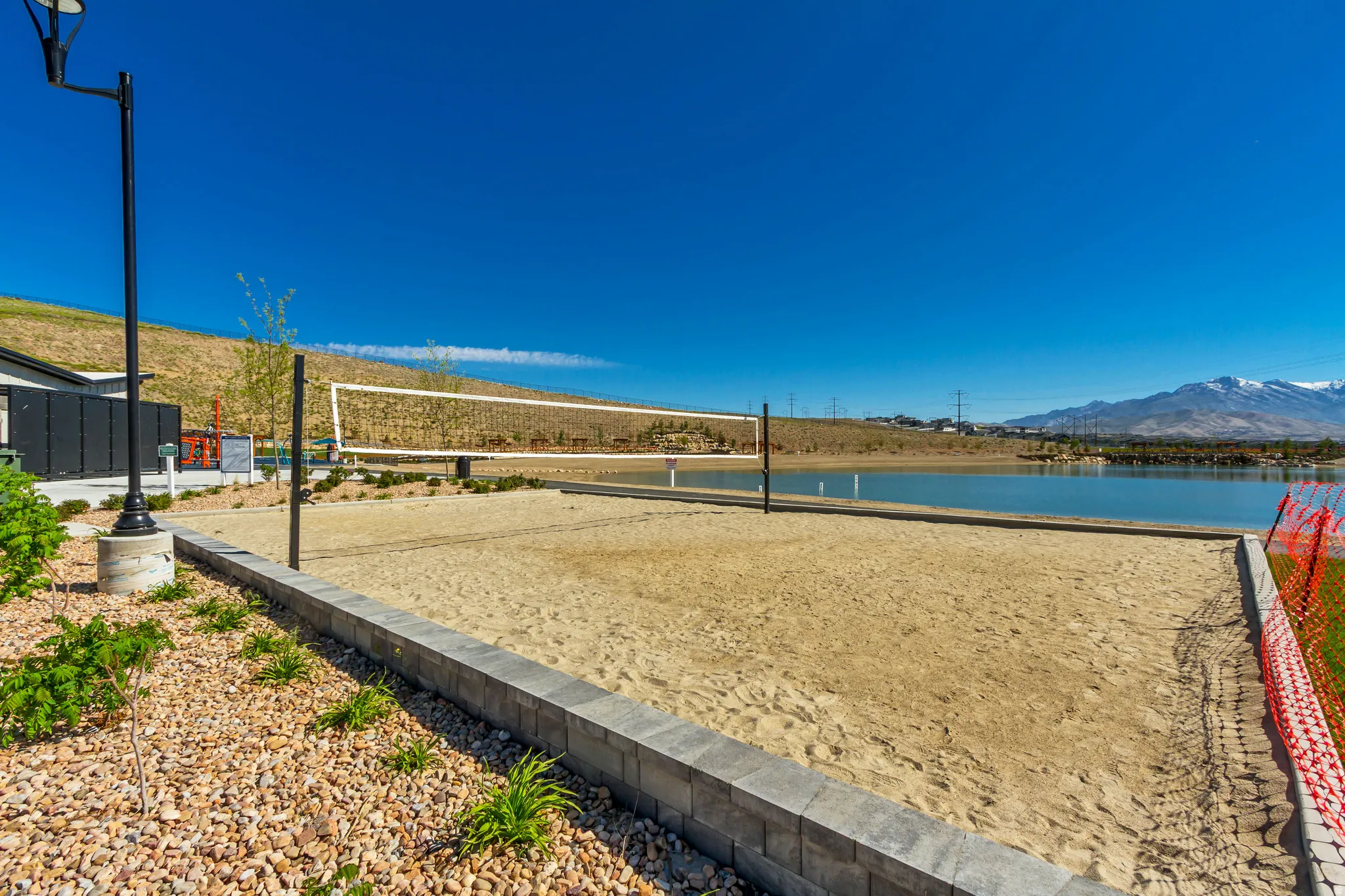 Sand volleyball court featuring a net and clear court lines, bordered by a paver retaining wall
