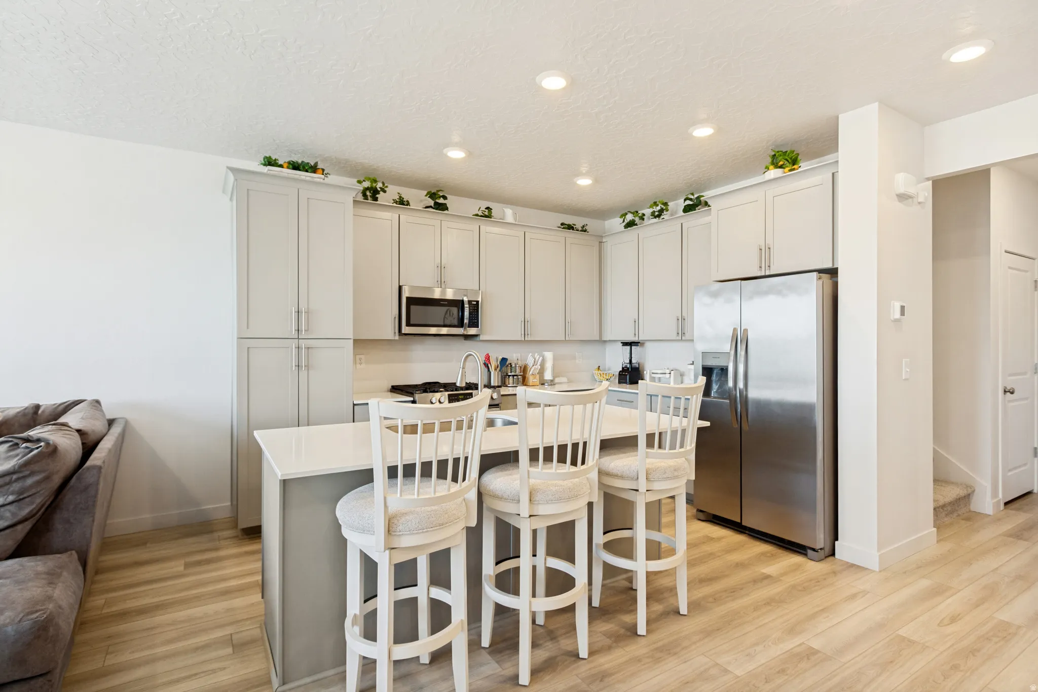 Modern kitchen featuring light gray cabinetry, stainless steel appliances, and a central island with a light-toned countertop