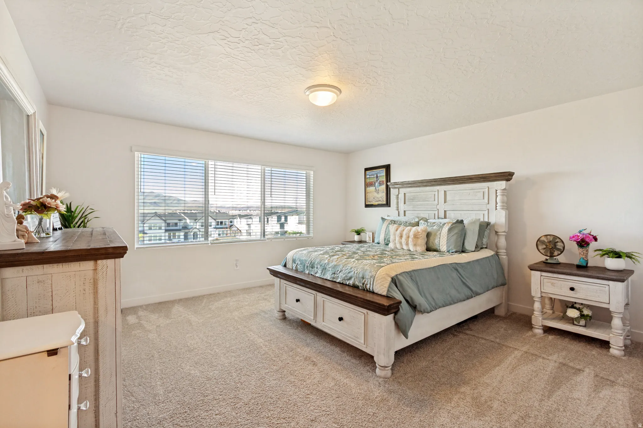 Carpeted bedroom with neutral white walls, a multi-pane window with horizontal blinds, and a ceiling-mounted light fixture