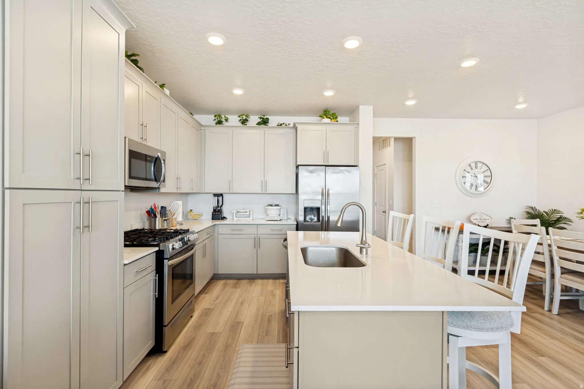 Modern kitchen featuring light cabinetry, stainless steel appliances, a center island with sink, quartz countertops, and wood-finish flooring