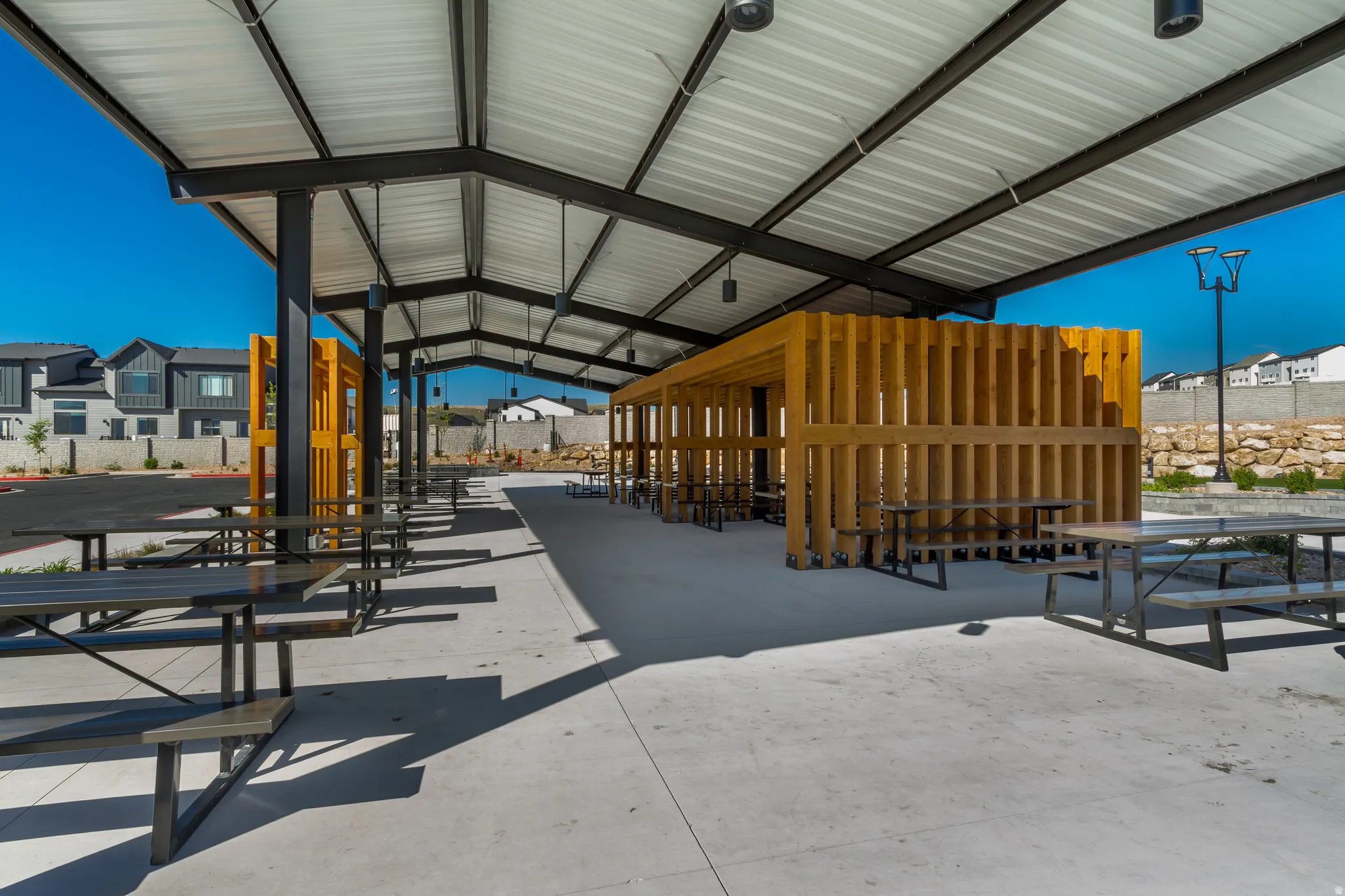 Covered outdoor pavilion featuring a metal roof structure, concrete flooring, and multiple picnic tables