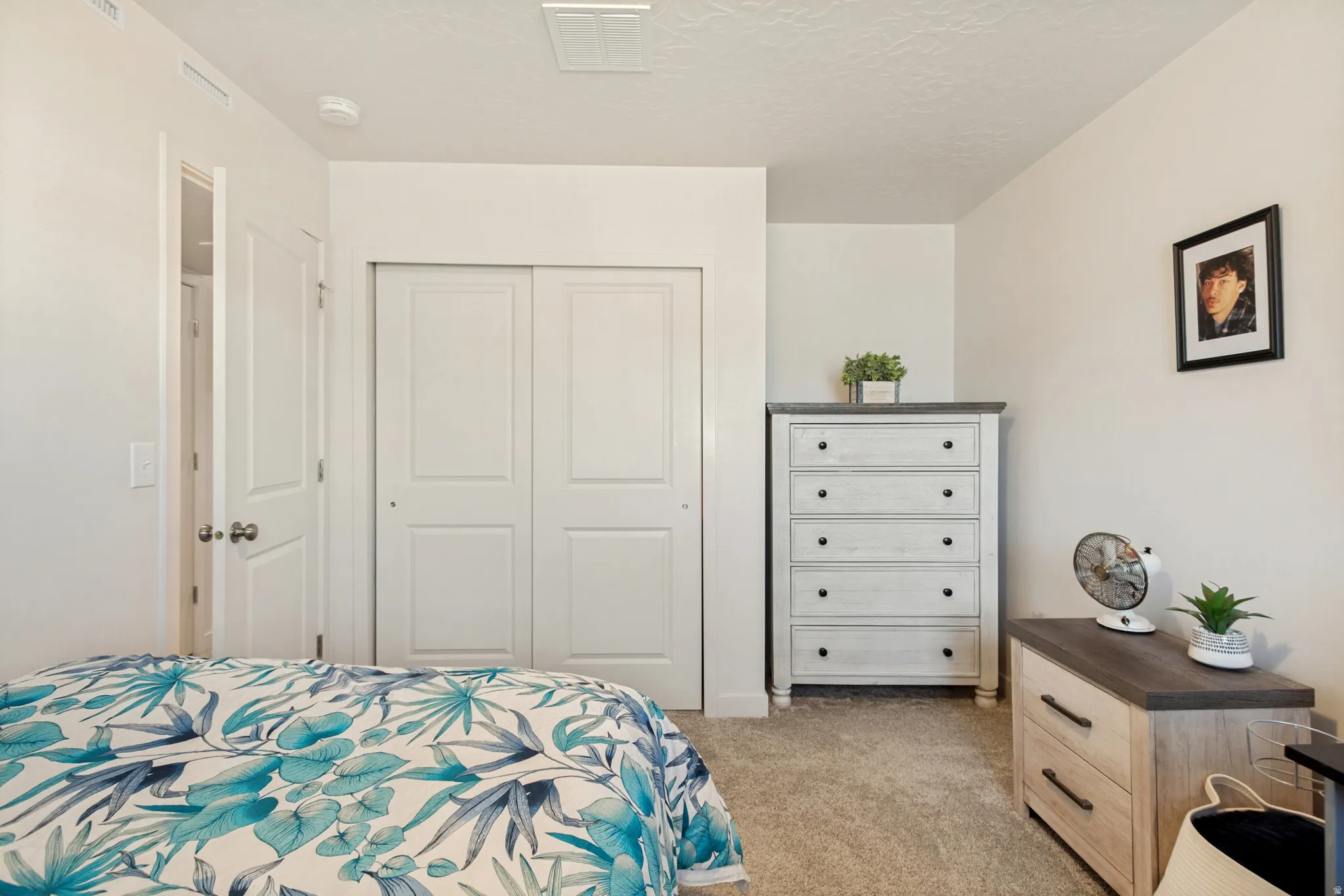 Carpeted room featuring a double-door closet with paneling, white walls, and a white ceiling with a visible vent