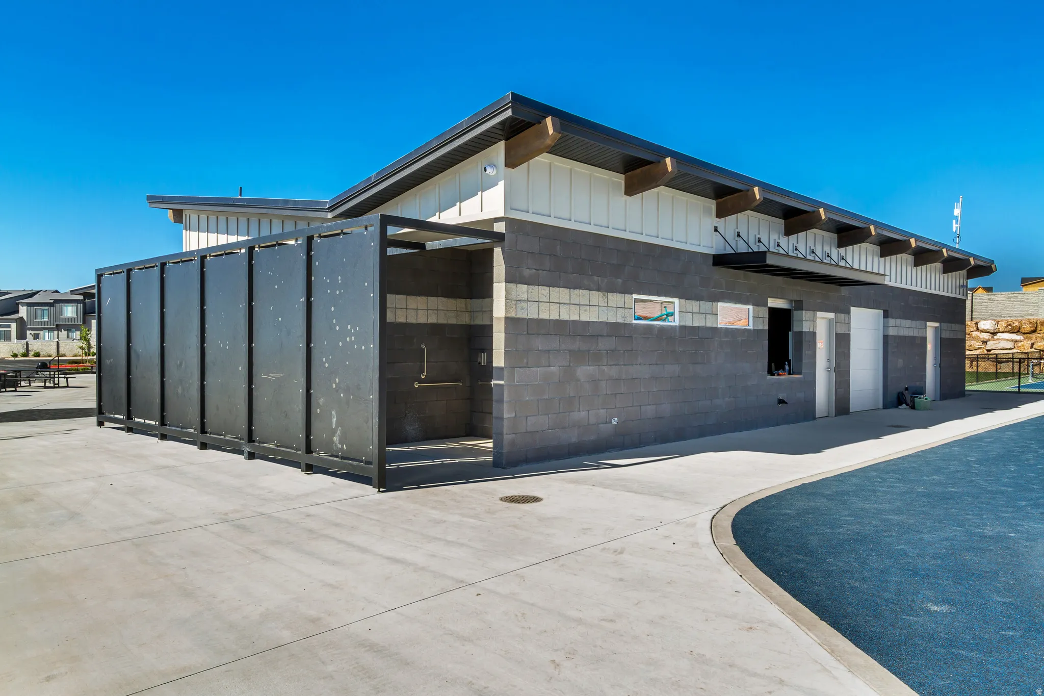Recreational building featuring a dark gray block facade, white vertical siding, exposed wood rafters, and a dark asphalt shingle roof