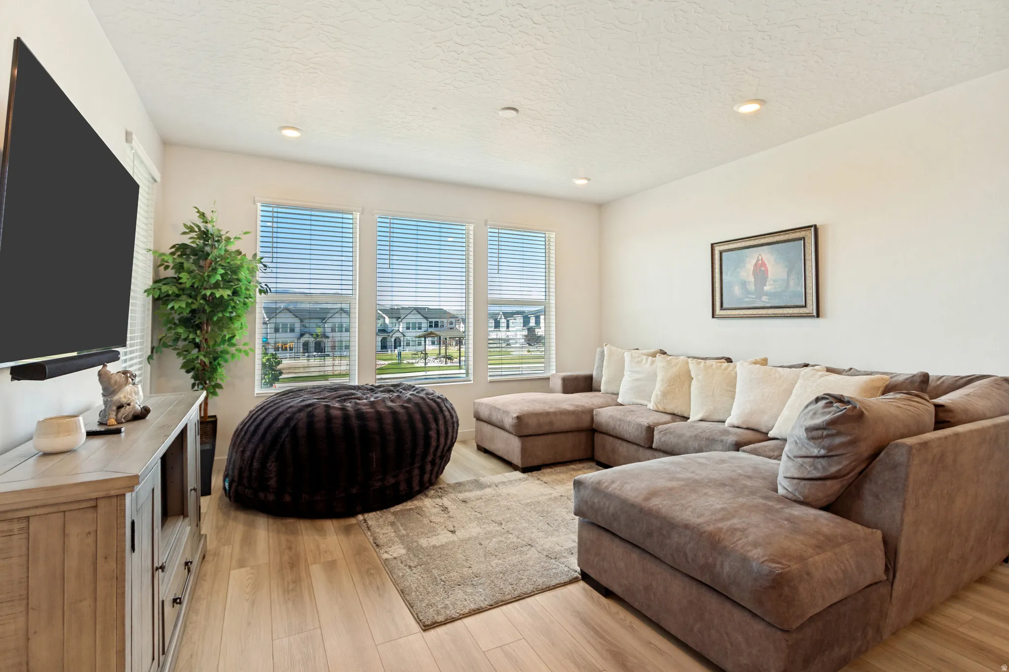 Living area featuring wood-finish flooring, recessed lighting, and large windows with blinds