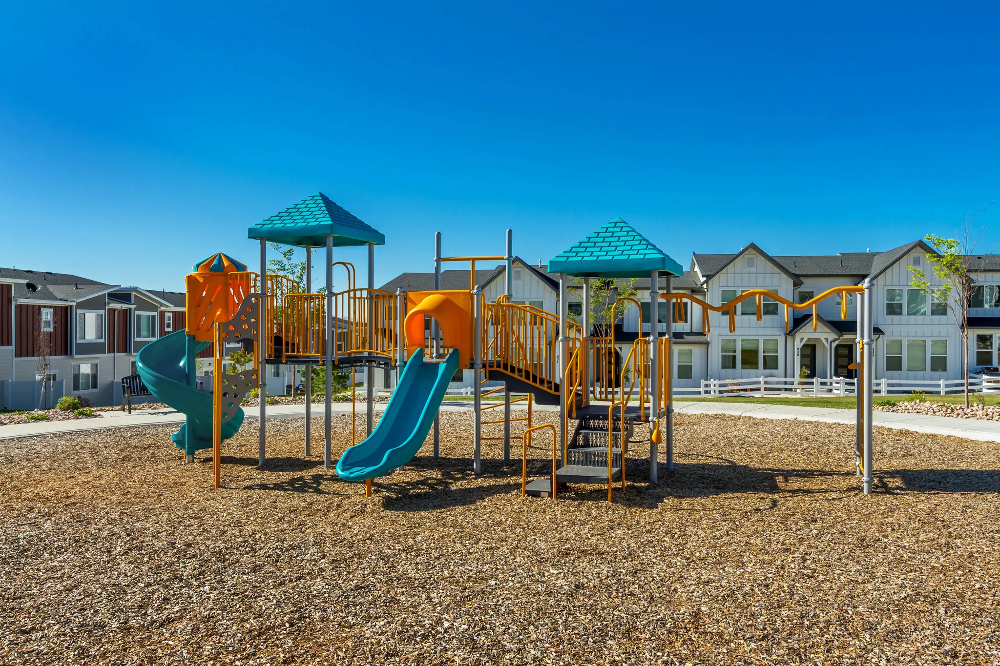 Community playground featuring multiple slides, climbing structures, and swings, set on a wood chip base