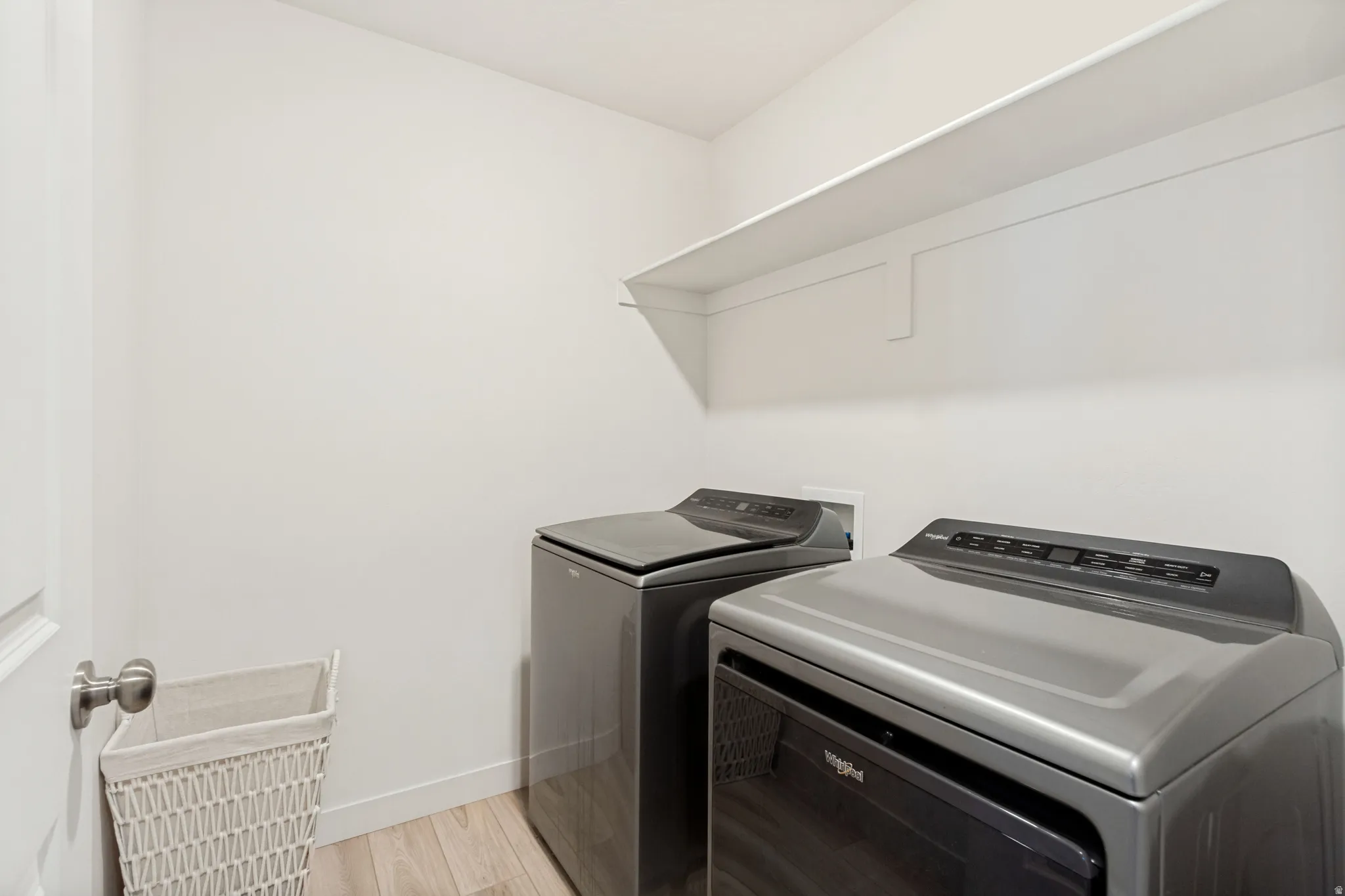 Dedicated laundry space featuring a floating shelf, wood-finish flooring, and white painted walls
