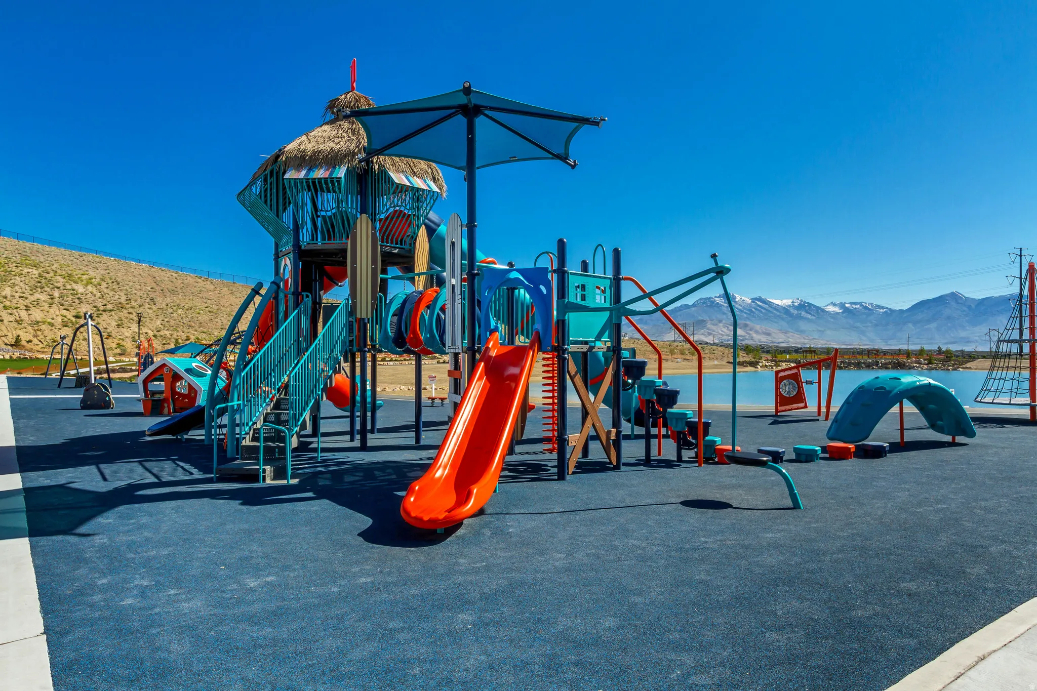 Community playground featuring a multi-level play structure with slides and tunnels, textured climbing elements, and a soft-surface ground cover