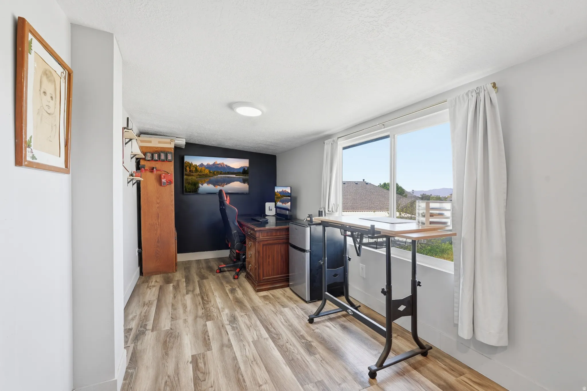 Spacious room featuring wood-finish flooring, a large window with white curtains, and an accent wall