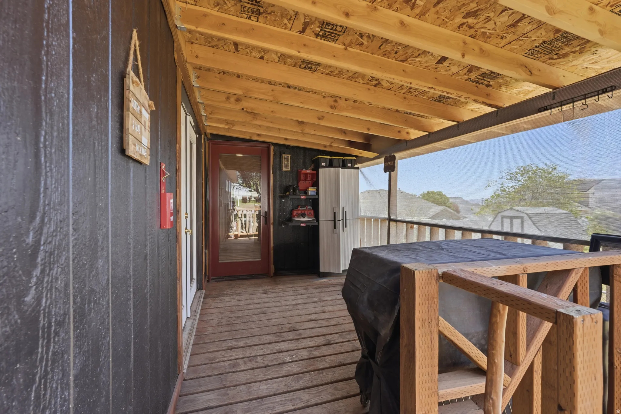 Covered outdoor deck with exposed wood beam ceiling, wood-plank flooring, and dark board-and-batten style siding