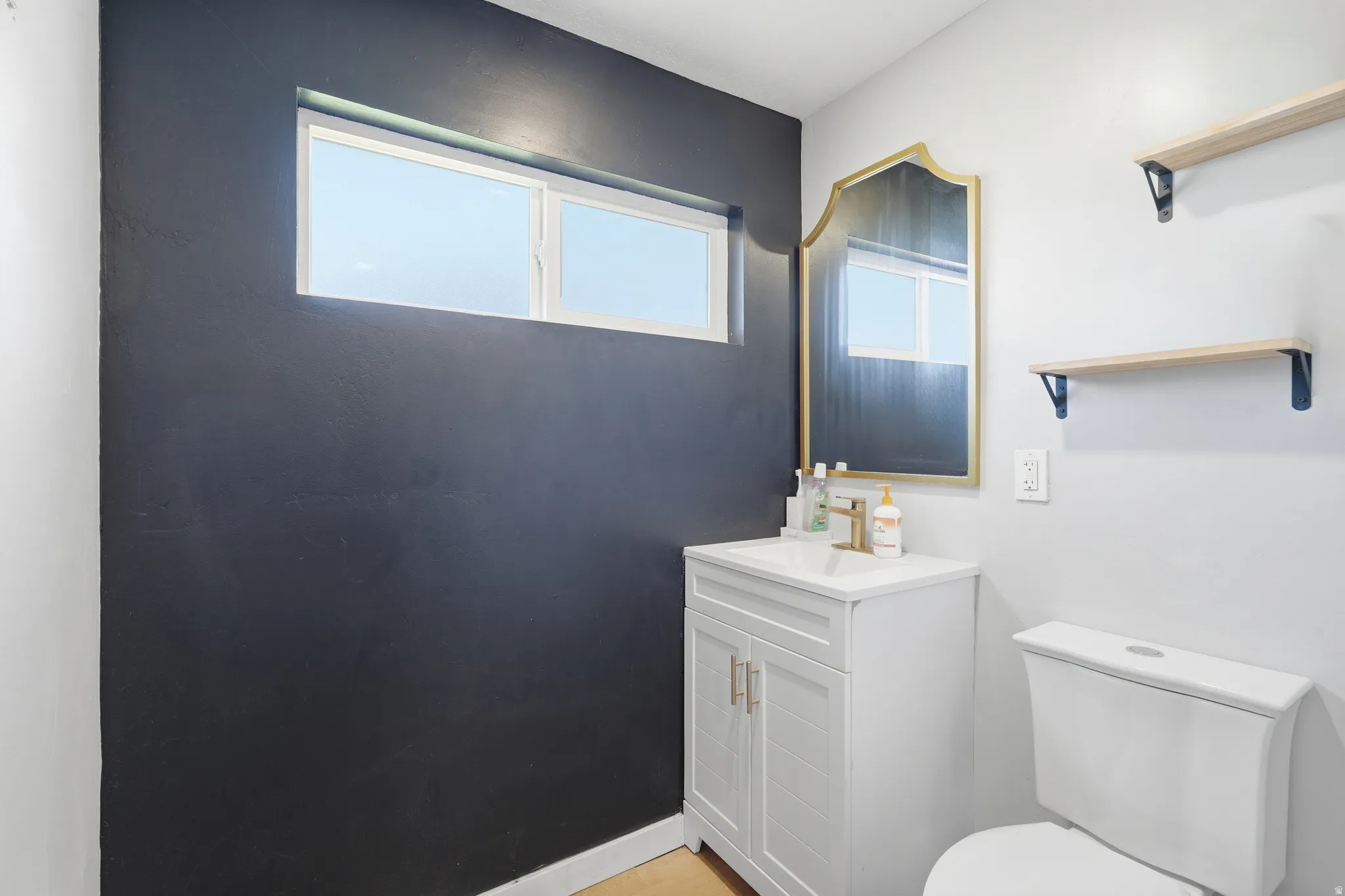Vanity with white shaker-style cabinetry and gold-tone hardware, a white rectangular sink, and gold-finish faucet
