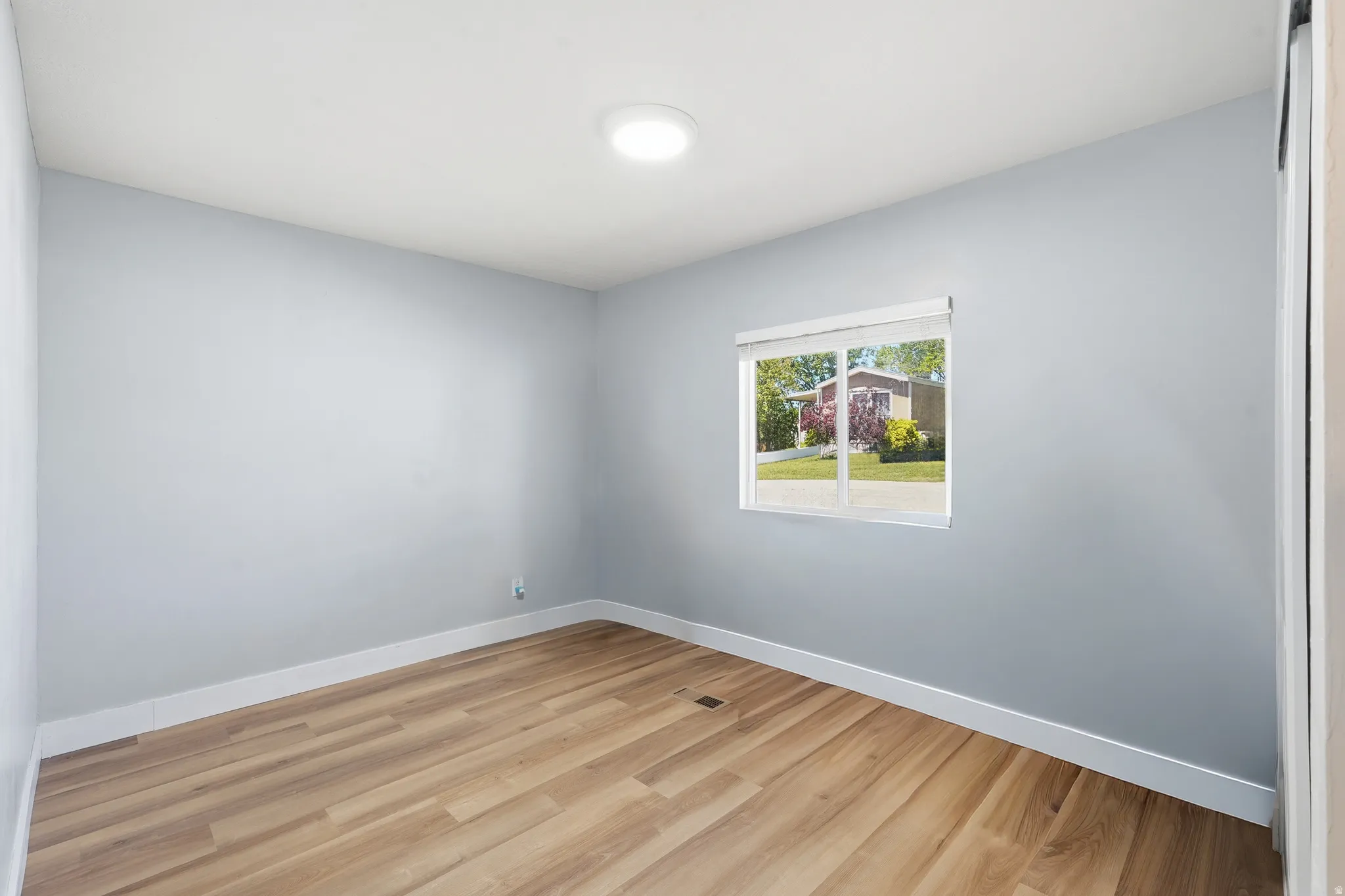 Spacious room featuring wood-finish flooring, light blue wall paint, white trim, and a window with white blinds