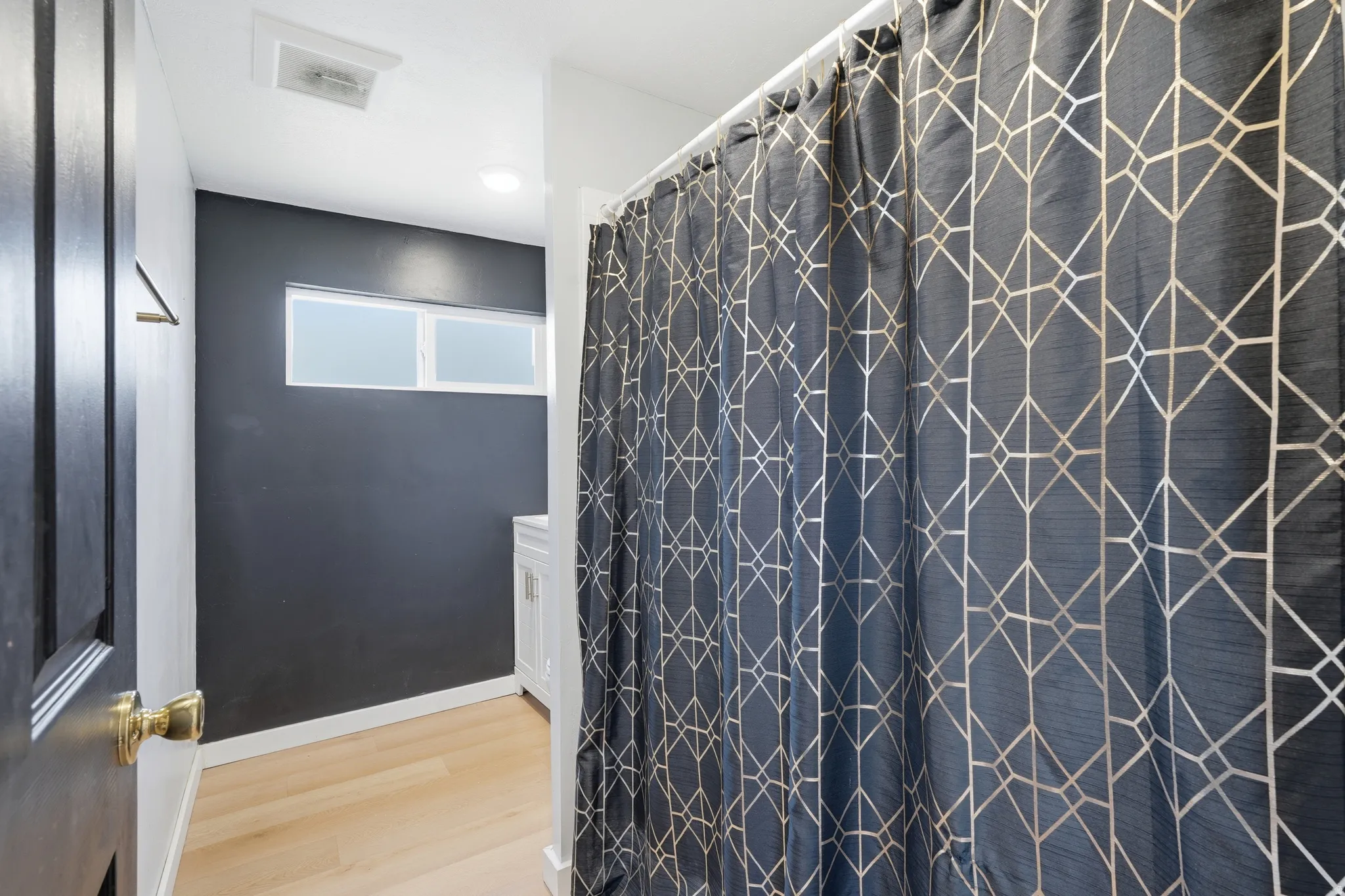 Bathroom featuring a shower with a patterned curtain, light wood-finish flooring, a contemporary vanity, and high horizontal windows
