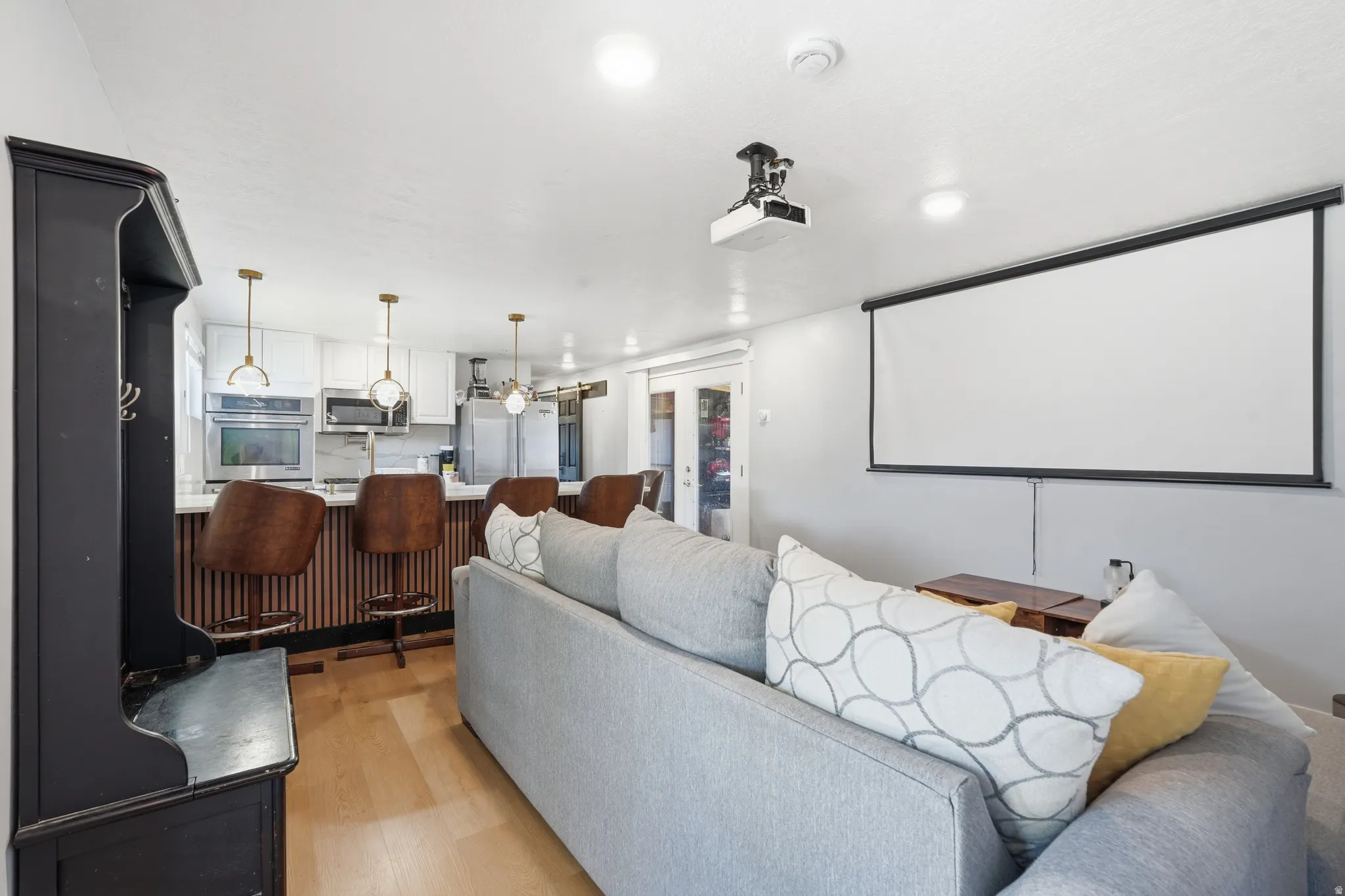 Open-concept living space featuring a built-in projector and screen, light wood-finish flooring, and white walls